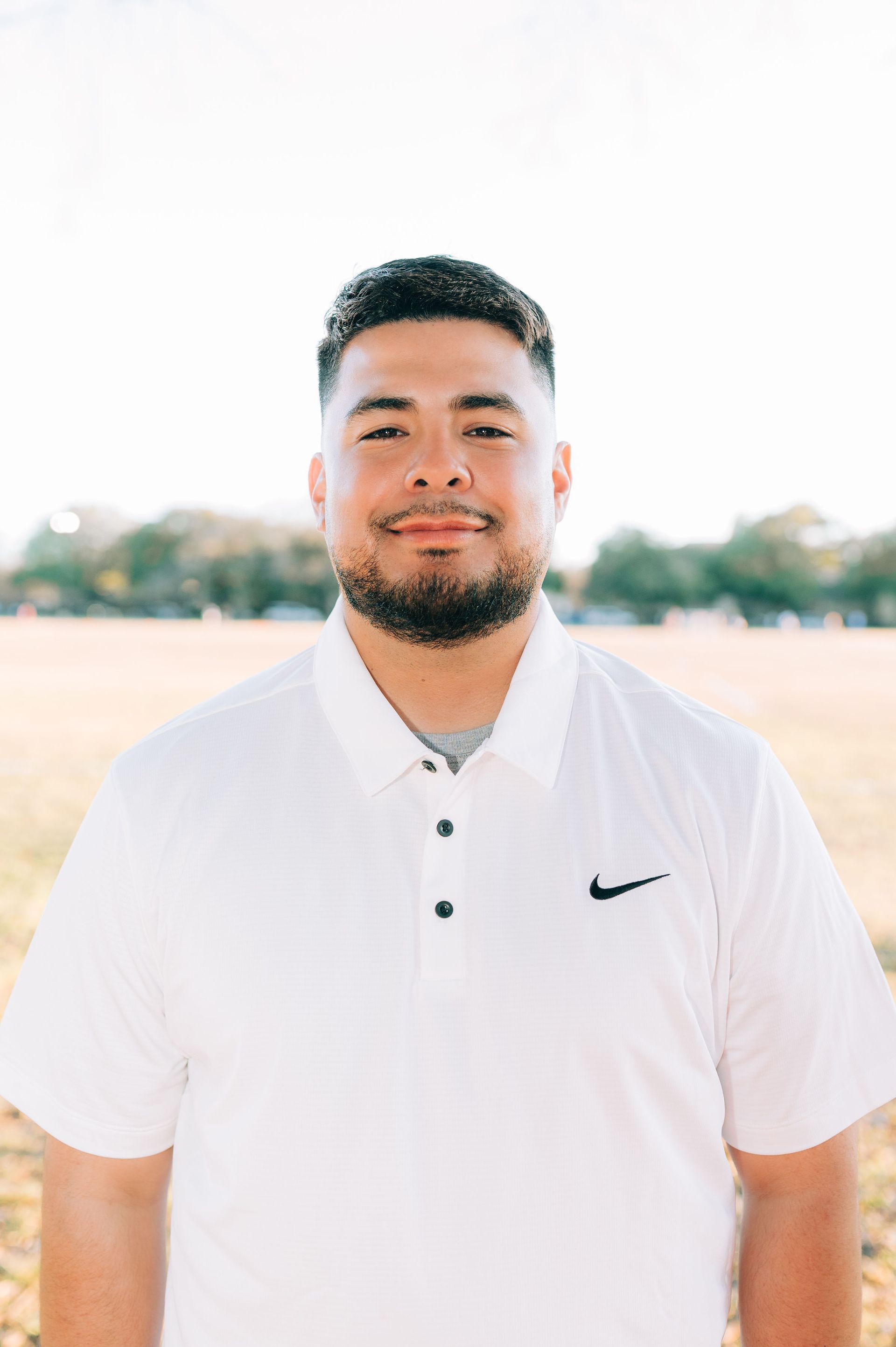 A man with a beard is wearing a white nike polo shirt.