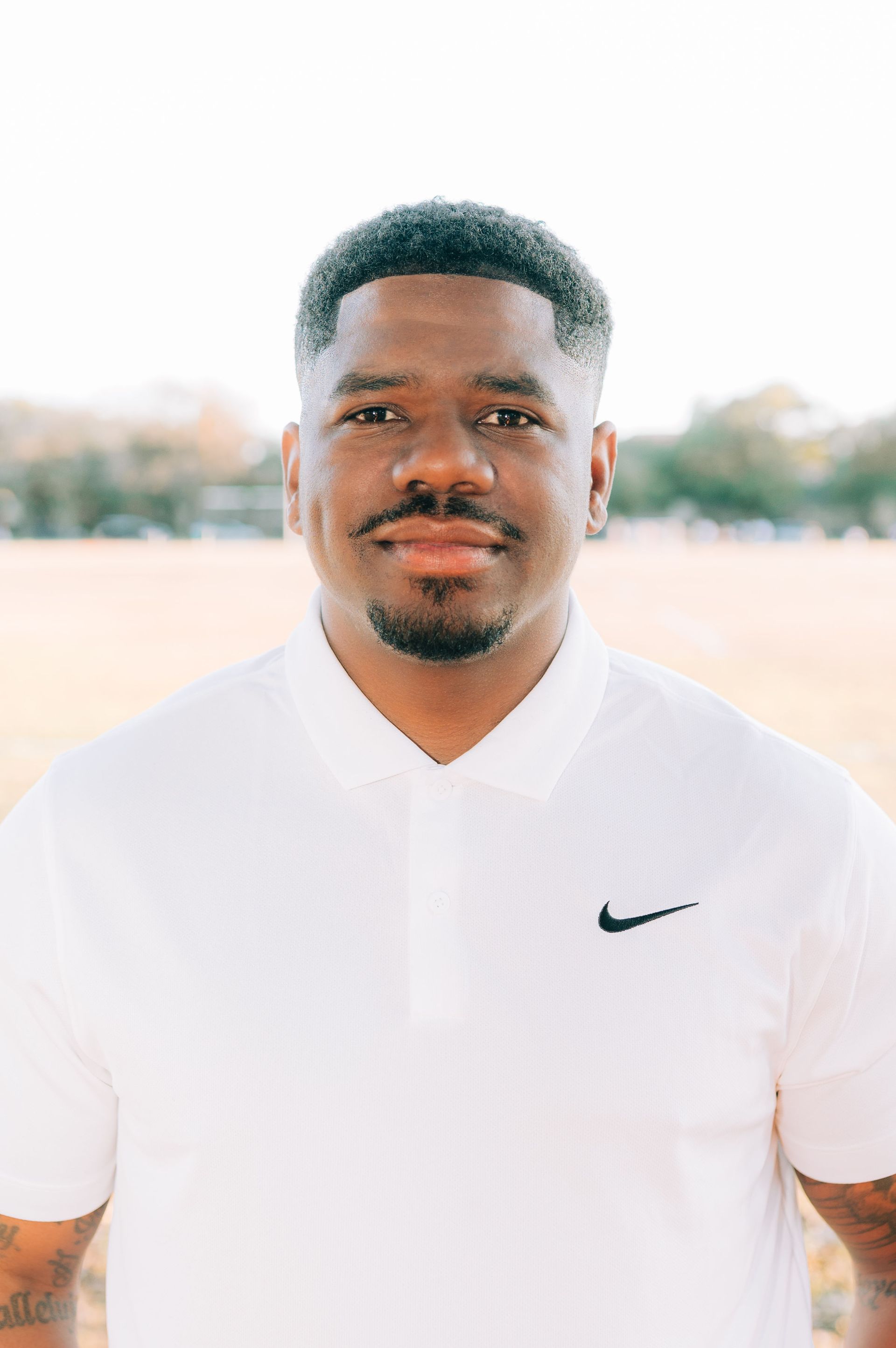 A man wearing a white nike polo shirt is standing in a field.