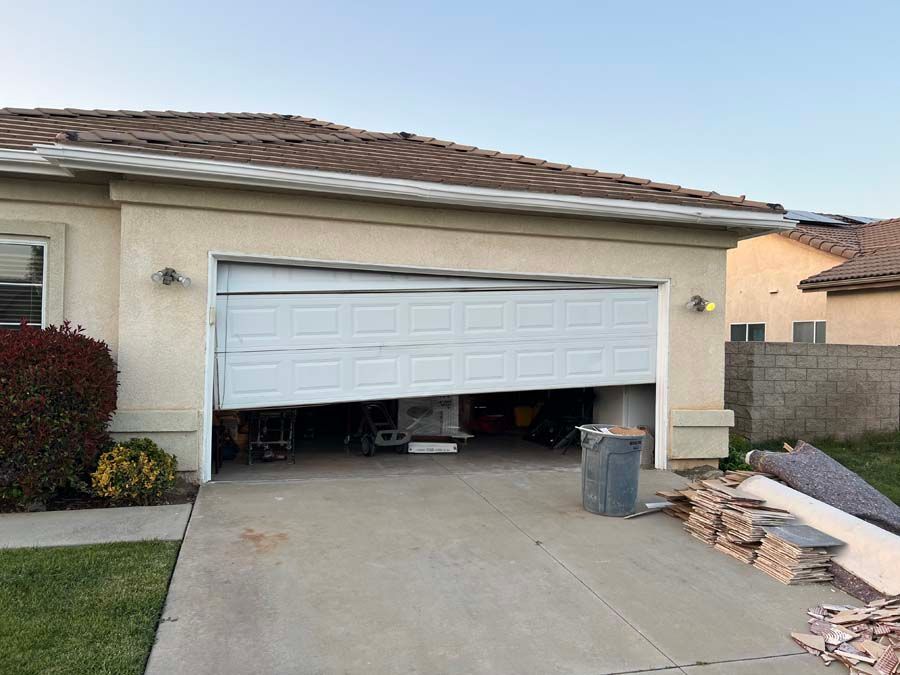 A garage door is open and broken in front of a house.