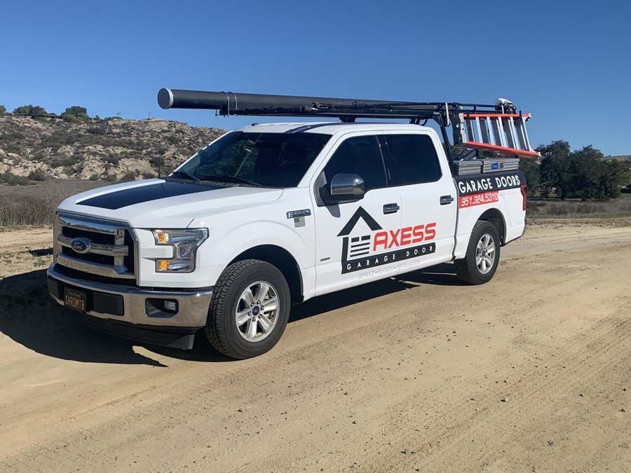 A white truck with a ladder on the back is parked on a dirt road.