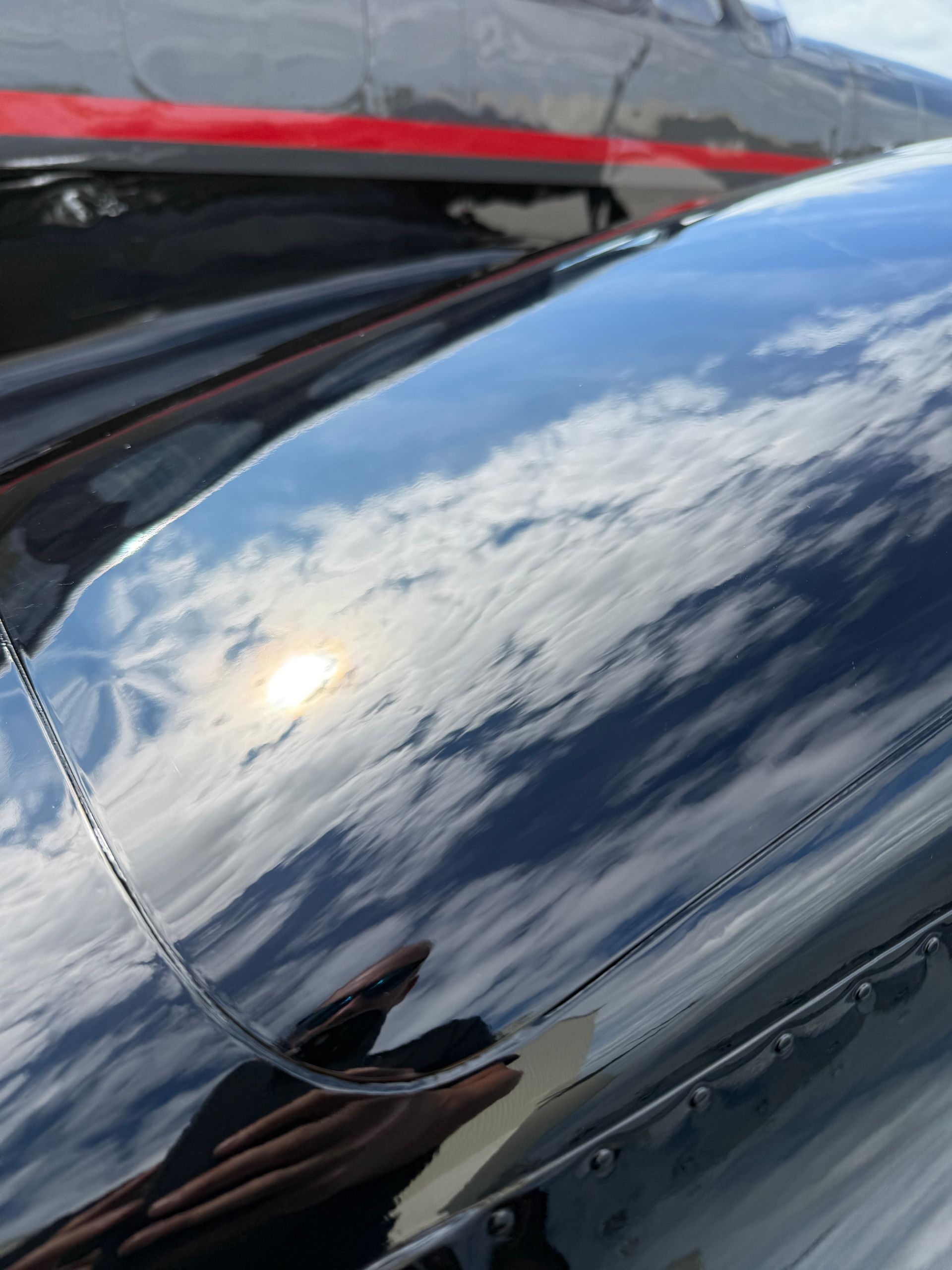 Black aircraft surface reflecting a sunny sky with clouds.