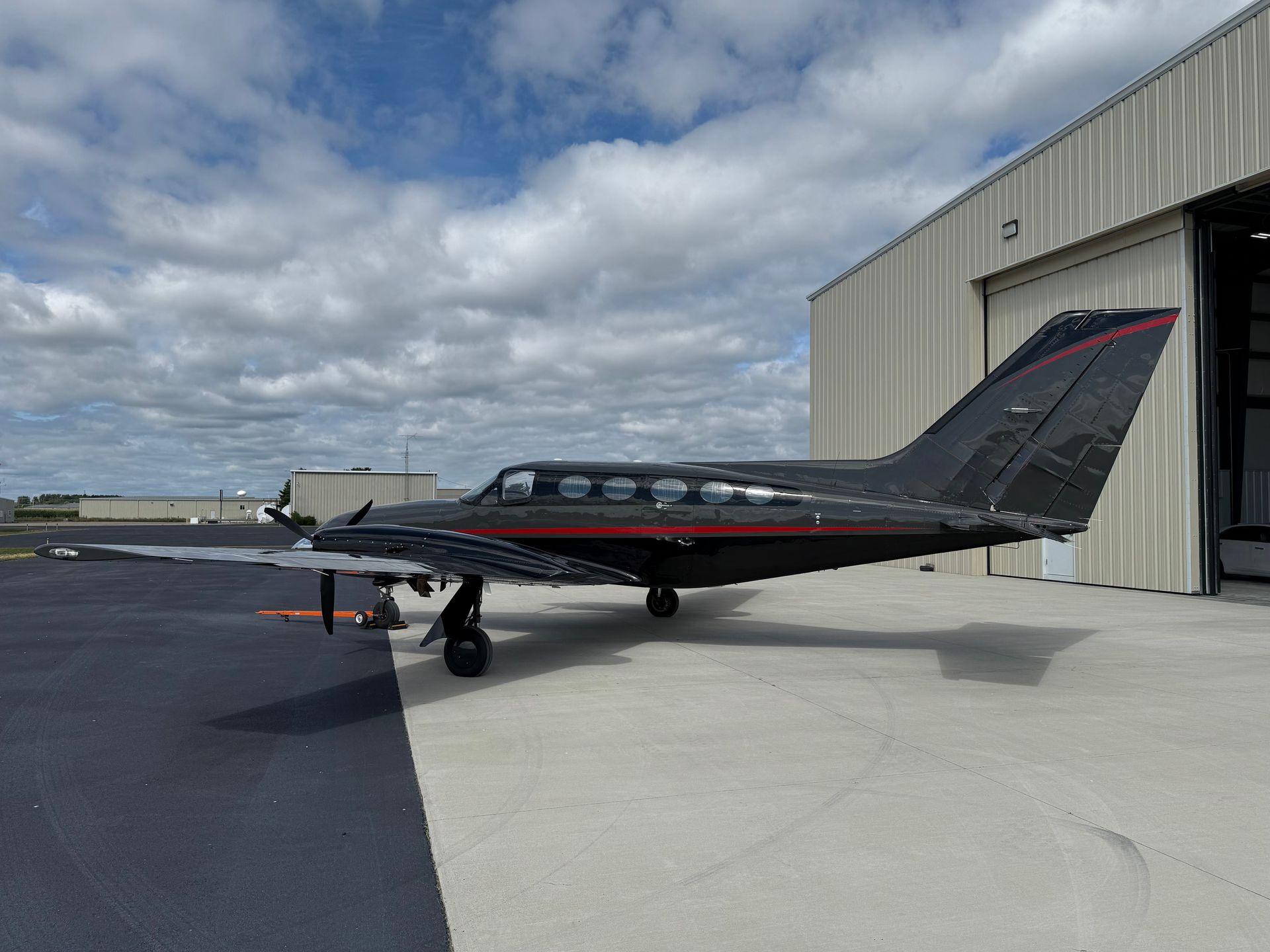 Black and red airplane parked on a tarmac in front of a hangar under a cloudy sky.