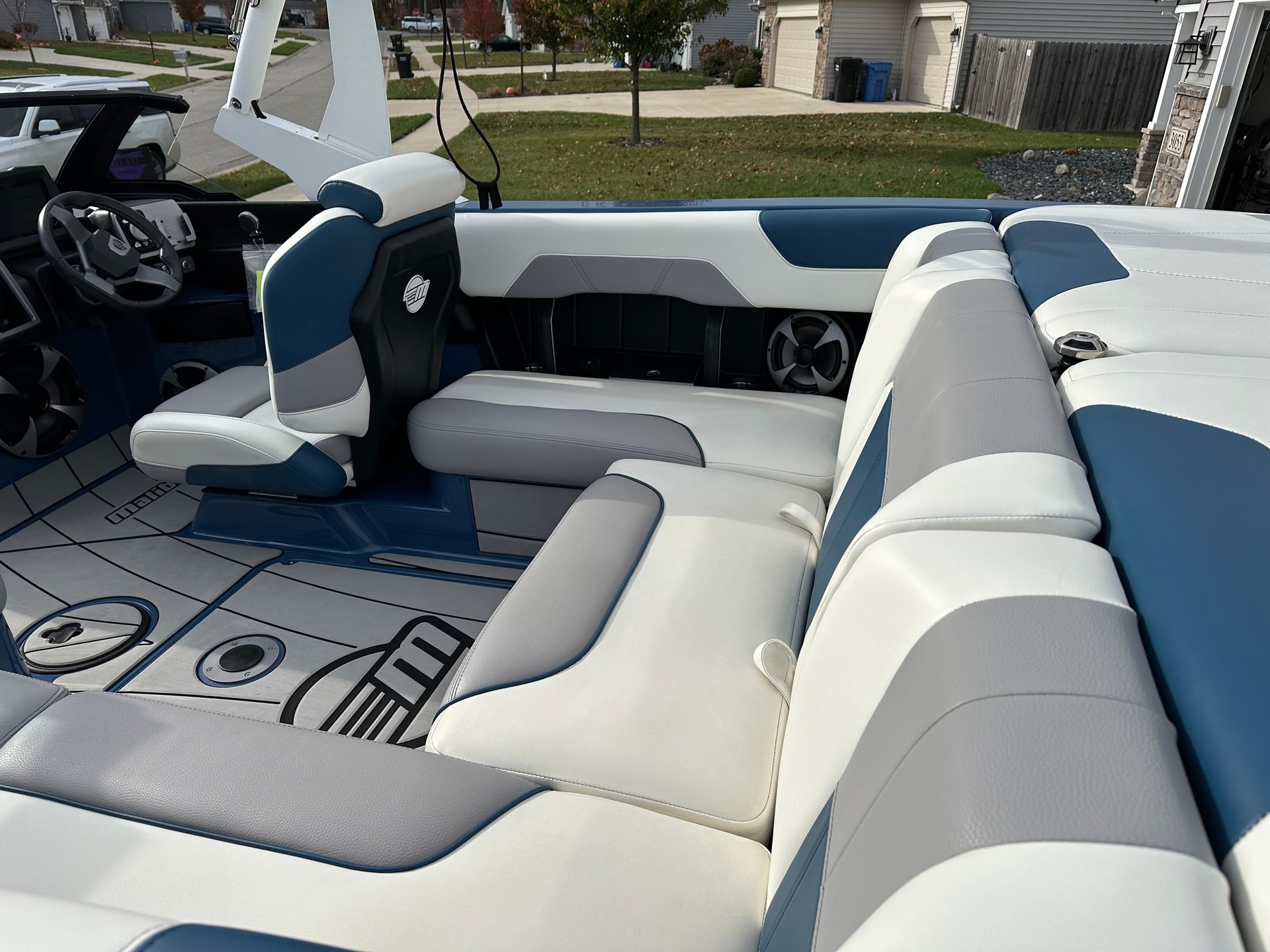 Boat interior with blue, white, and gray seating. Steering wheel, speaker, and patterned flooring visible.
