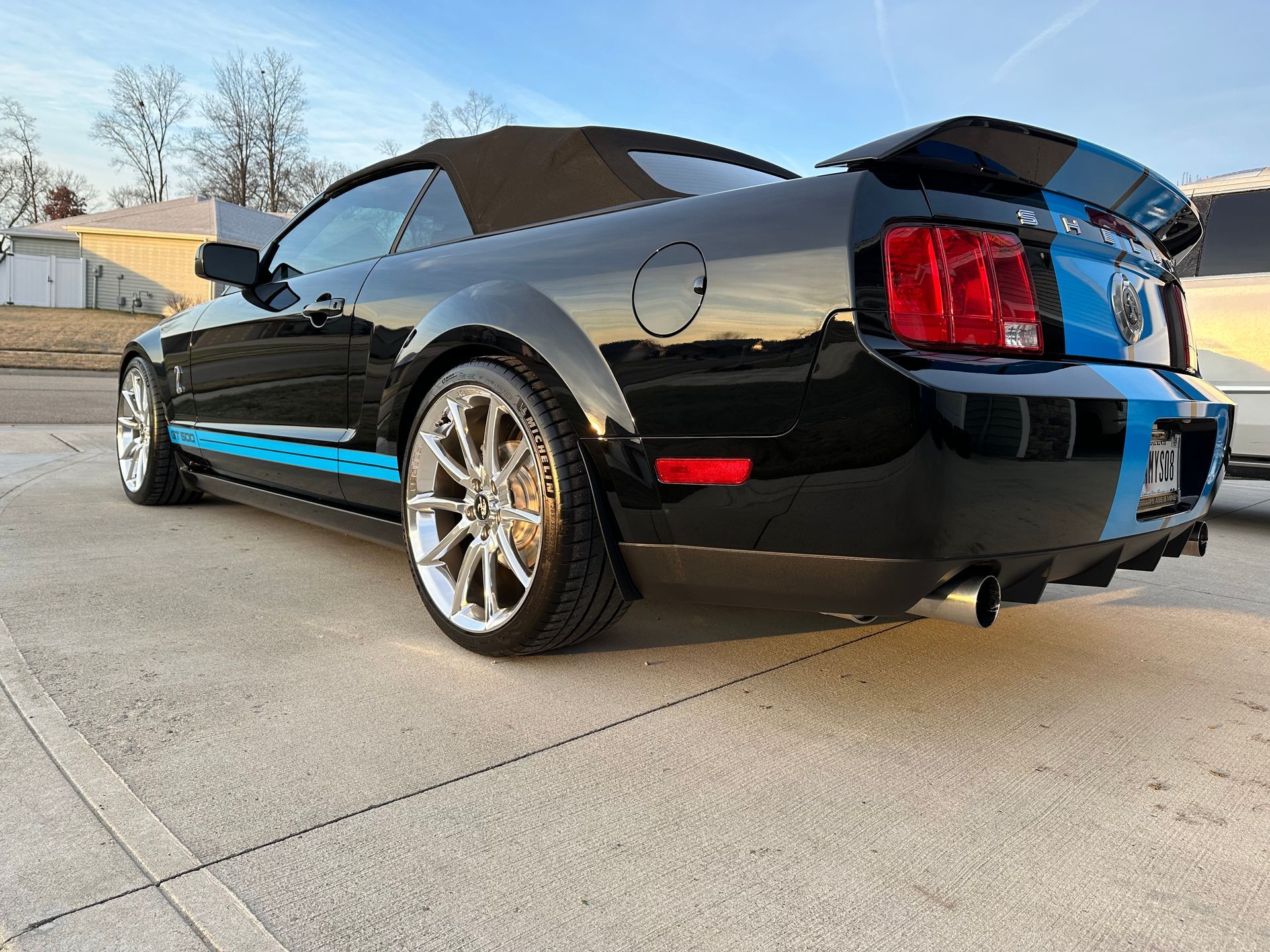 Black convertible Mustang with blue racing stripes, parked on concrete.