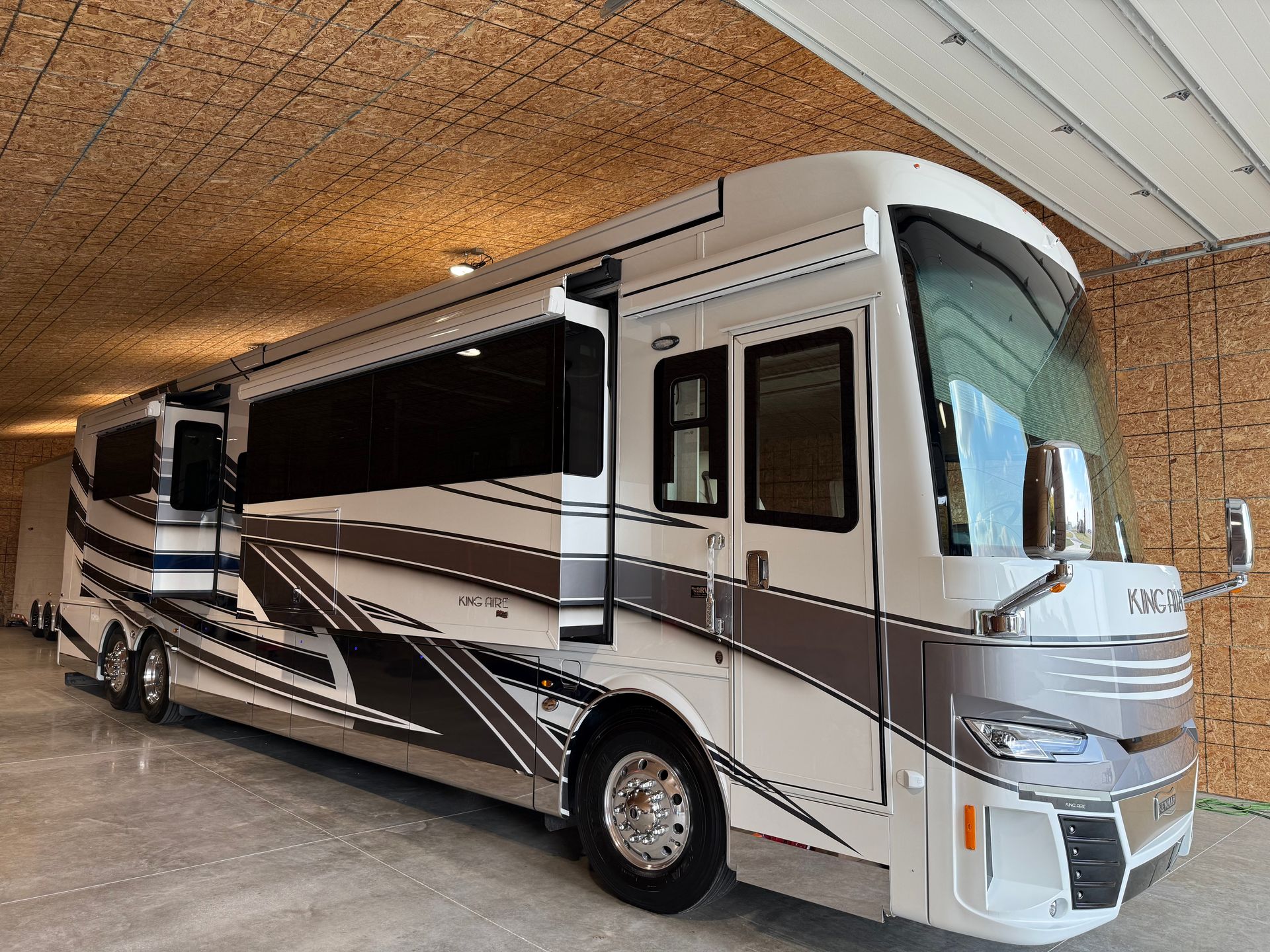 White and gray RV parked inside a building with a wood-paneled ceiling. Side door is open.