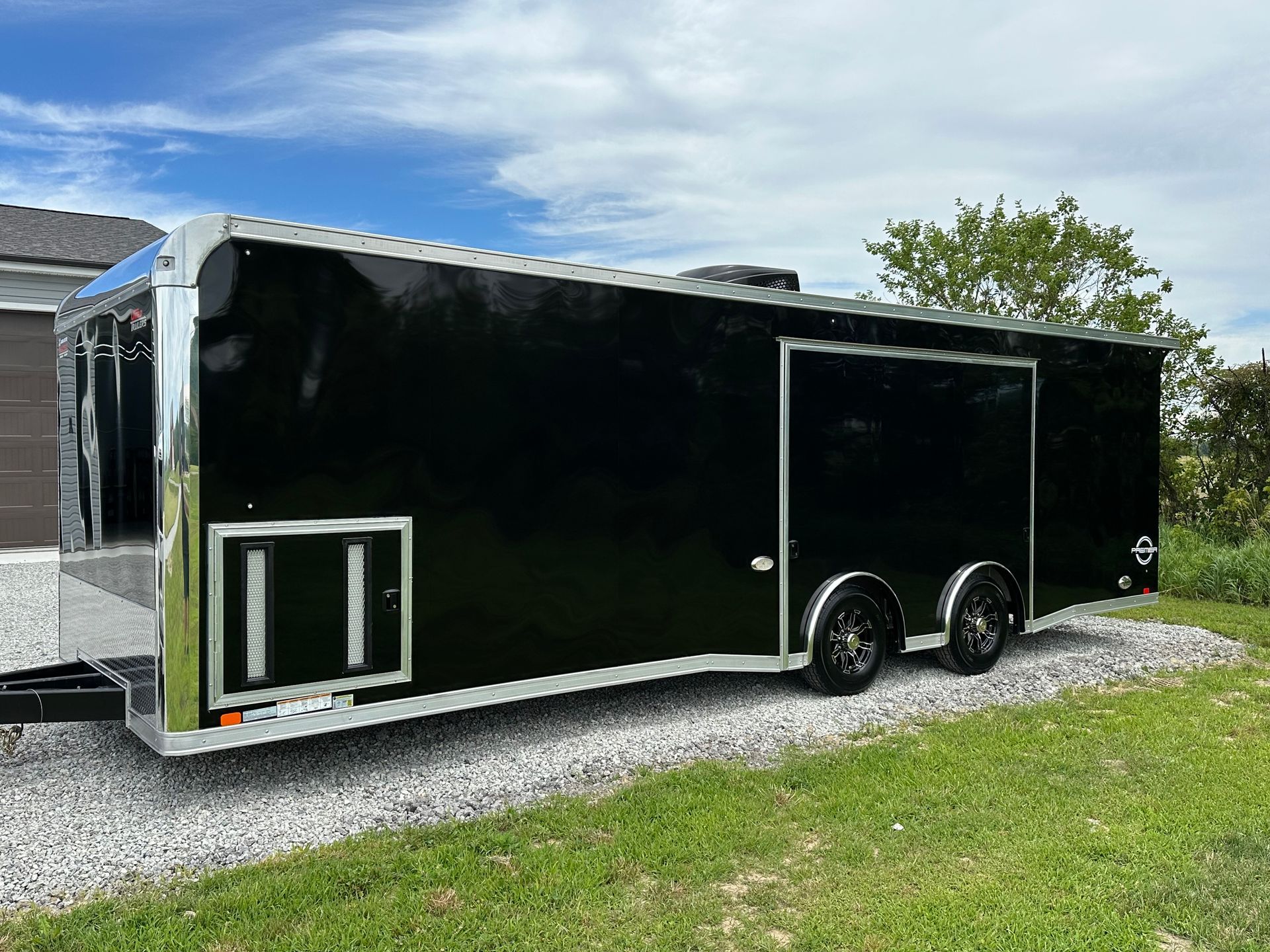 Black enclosed trailer on gravel with a cloudy sky in the background.