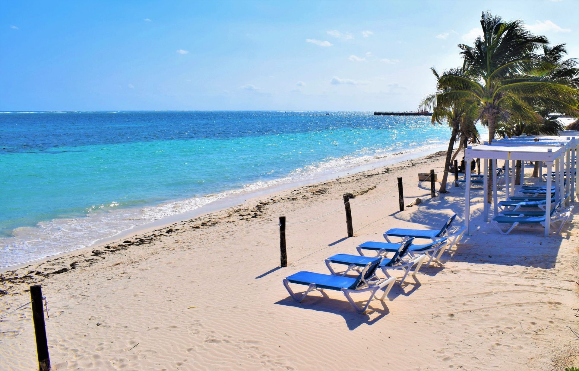 Beach with turquoise water, white sand, and blue lounge chairs under a blue sky.