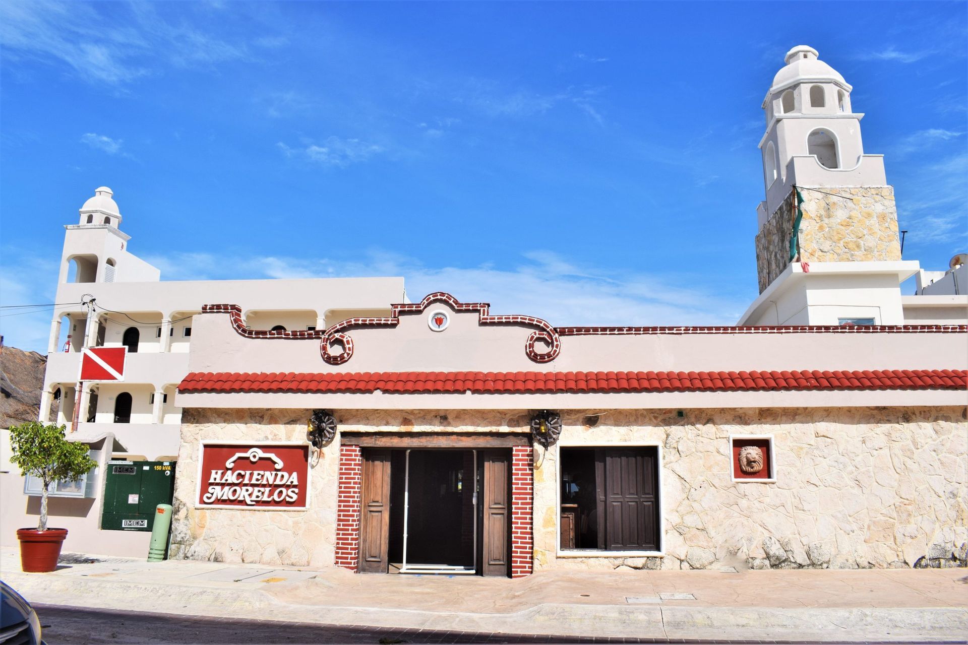 Hacienda Paradise hotel exterior with white walls, red roof trim, and a blue sky.