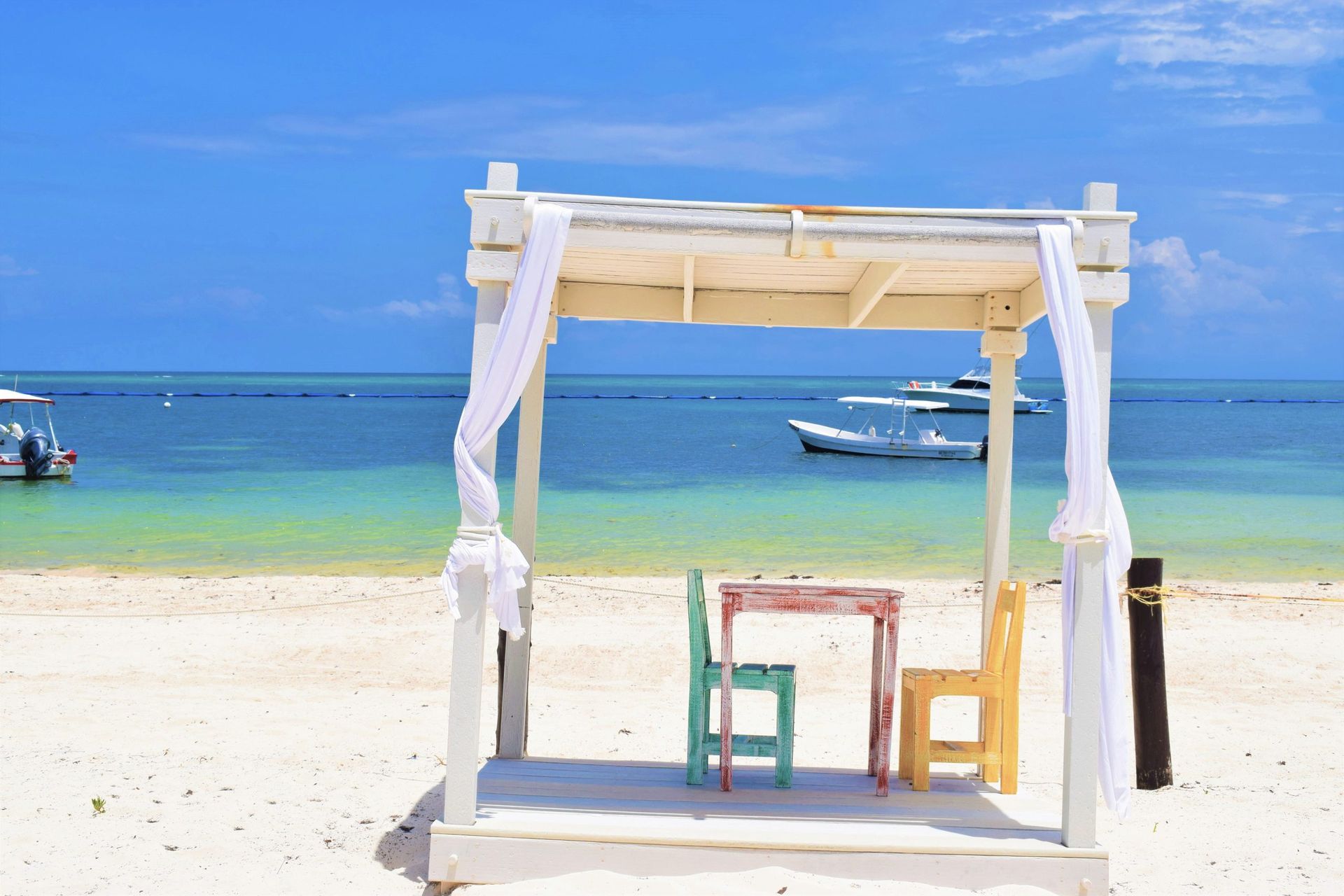 Beach cabana with table and chairs, ocean view, blue sky.