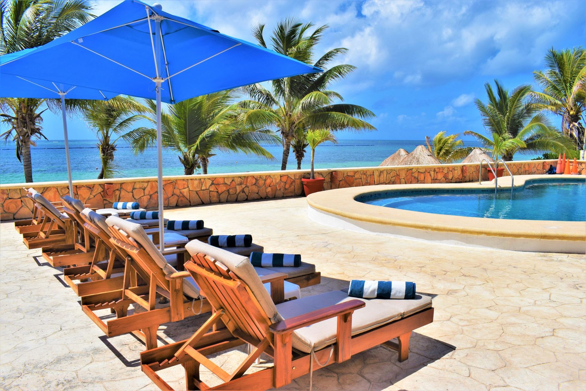 Tumbonas y piscina bajo una sombrilla azul junto al océano en un día soleado.