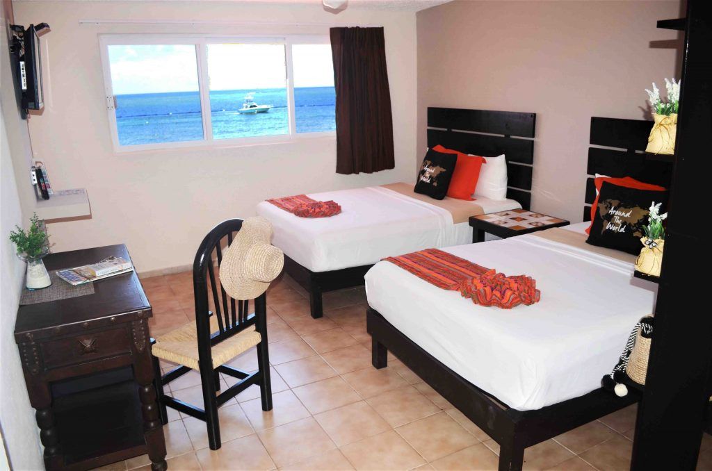 Dormitorio con dos camas individuales, vista al mar, escritorio con silla y televisión.
