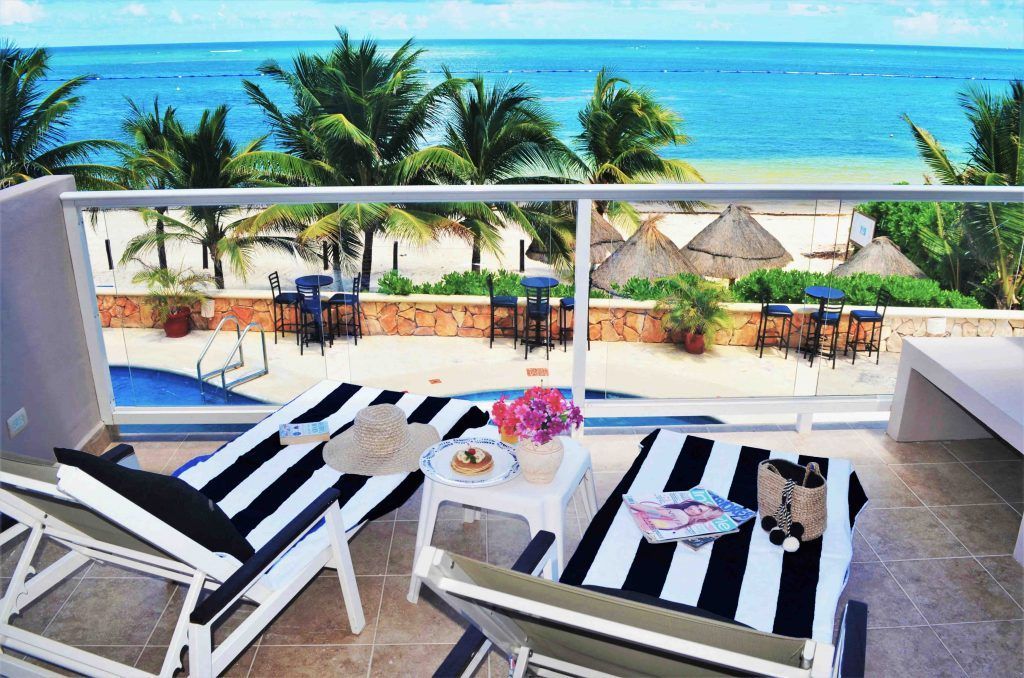 Balcón con vista a la playa: tumbonas, snacks, palmeras, mar.