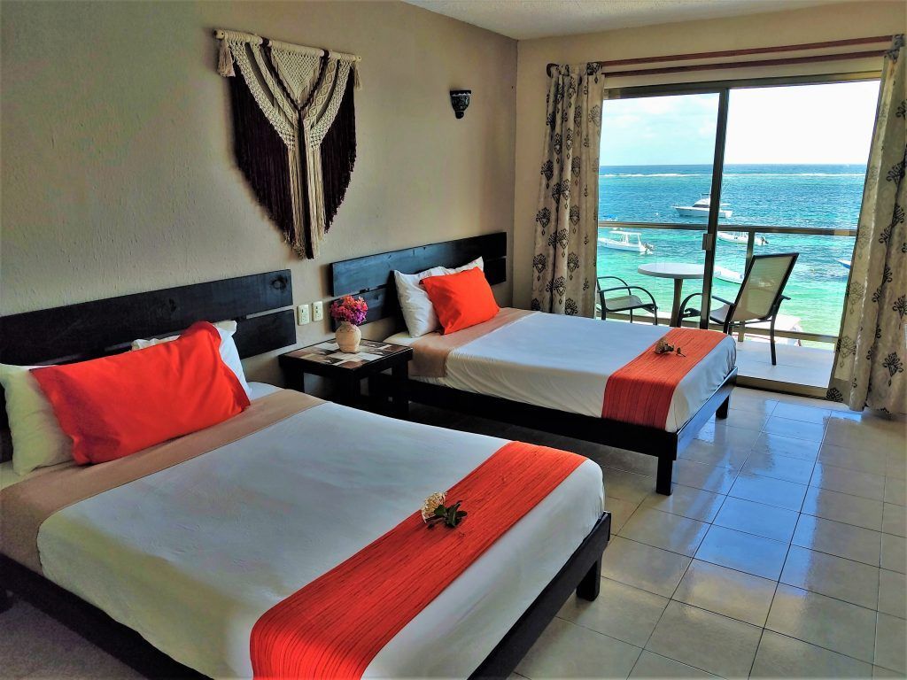 Dos camas individuales en una habitación de hotel con vista al mar desde el balcón.