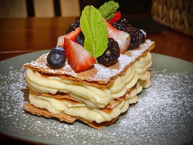 Napoléon pastry with layers of cream and puff pastry, topped with berries and mint on a plate.