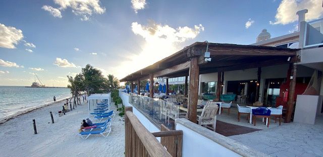 Beachside restaurant with tables, chairs, and ocean view under a cloudy sky.
