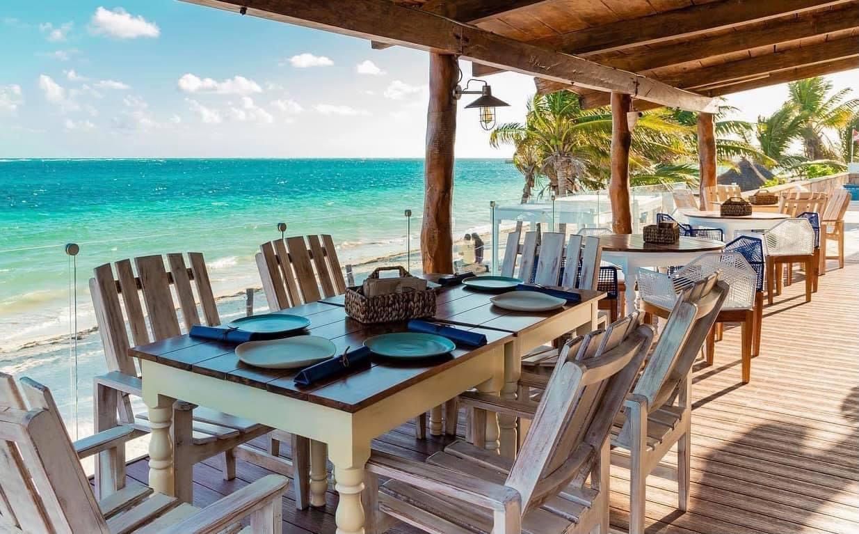 Beachside restaurant with tables set for dining, overlooking turquoise ocean.