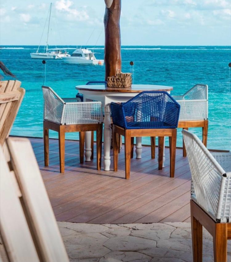 Dining table and chairs on a deck, with ocean and boats in background.