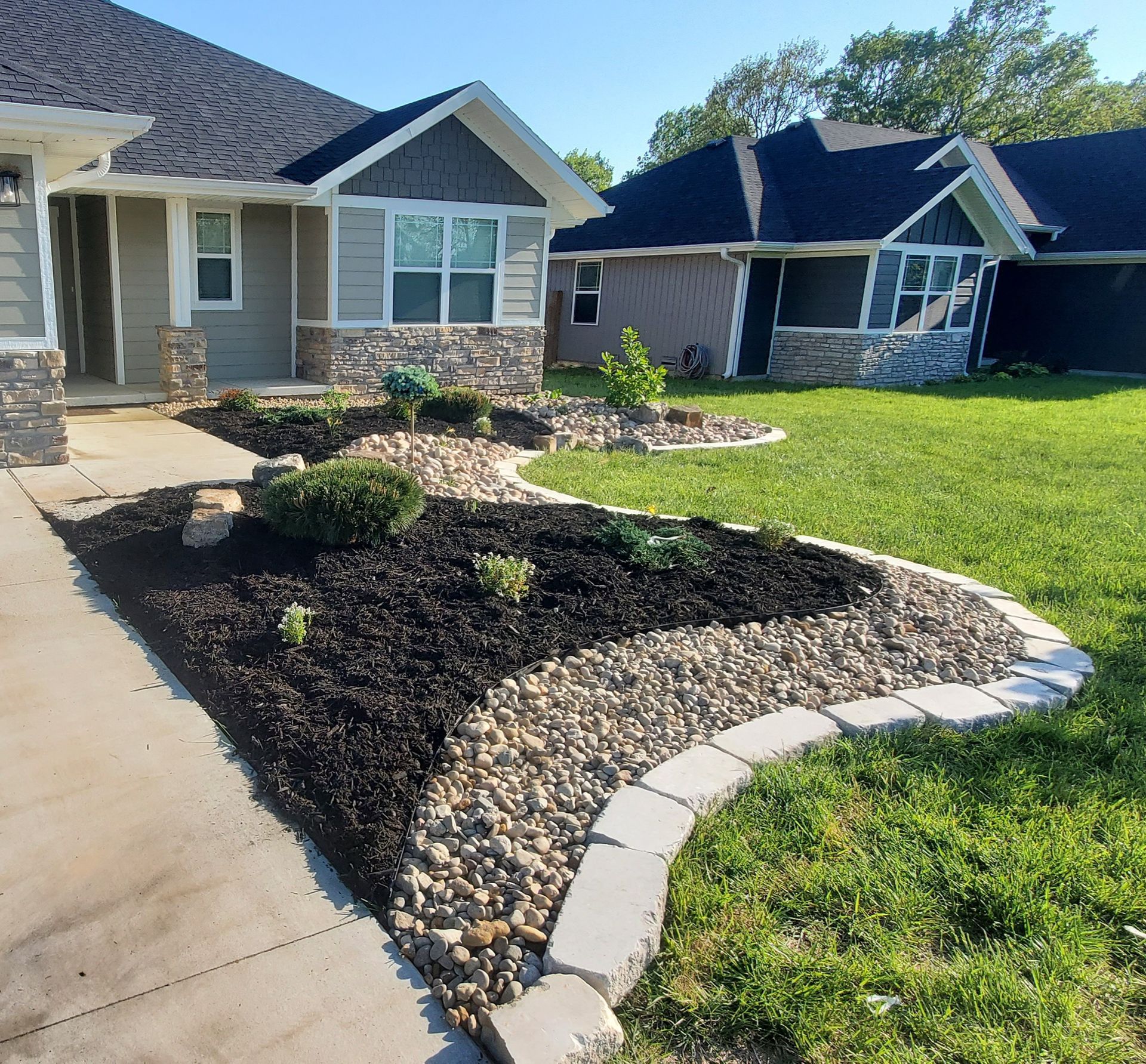 Brown and red Japanese maple in a gravel garden bed next to a house with a wooden deck and a driveway.