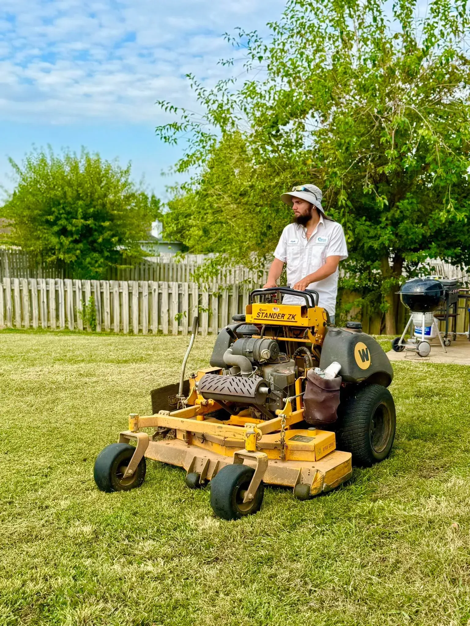 A person mowing a lawn with a yellow riding mower on a sunny day.