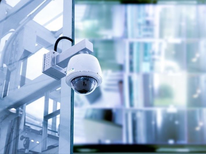 A security camera is hanging from the side of a building.