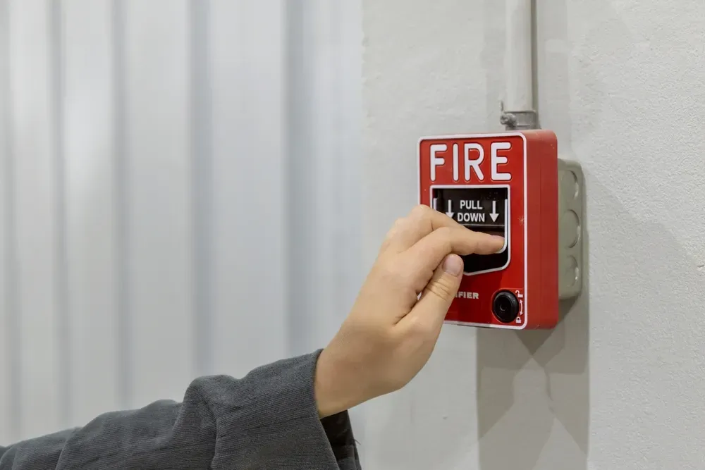 A person is pressing a fire alarm button on a wall.