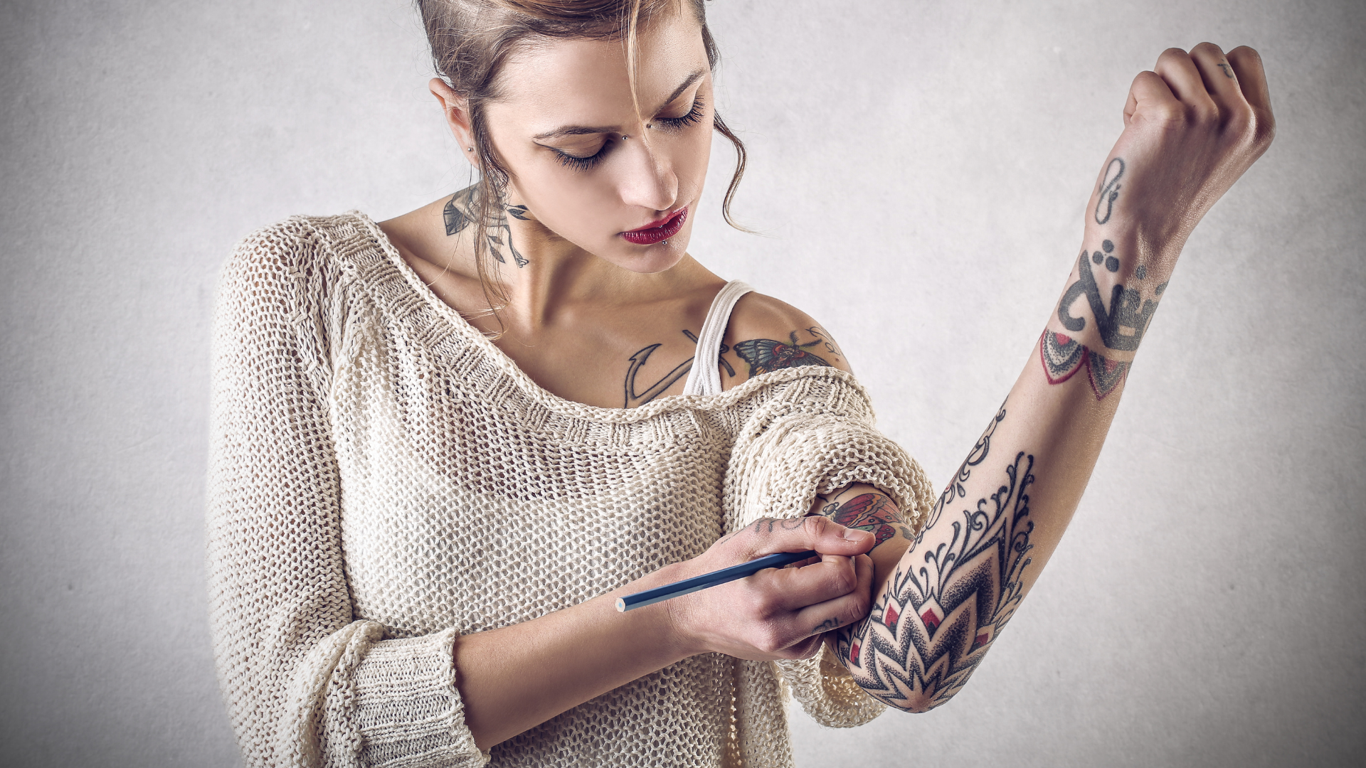 Woman with tattoos, drawing on arm with a pen.