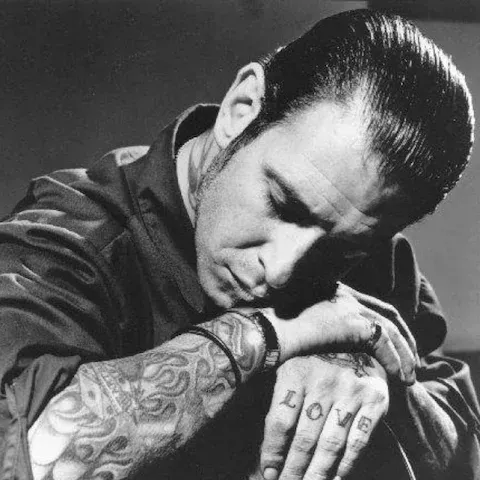 Man with tattoos, head resting on folded arms, hands showing 
