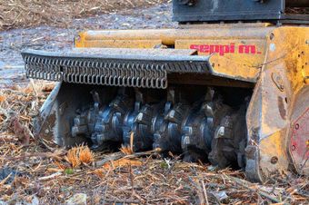 A close up of a machine that is cutting a tree stump.