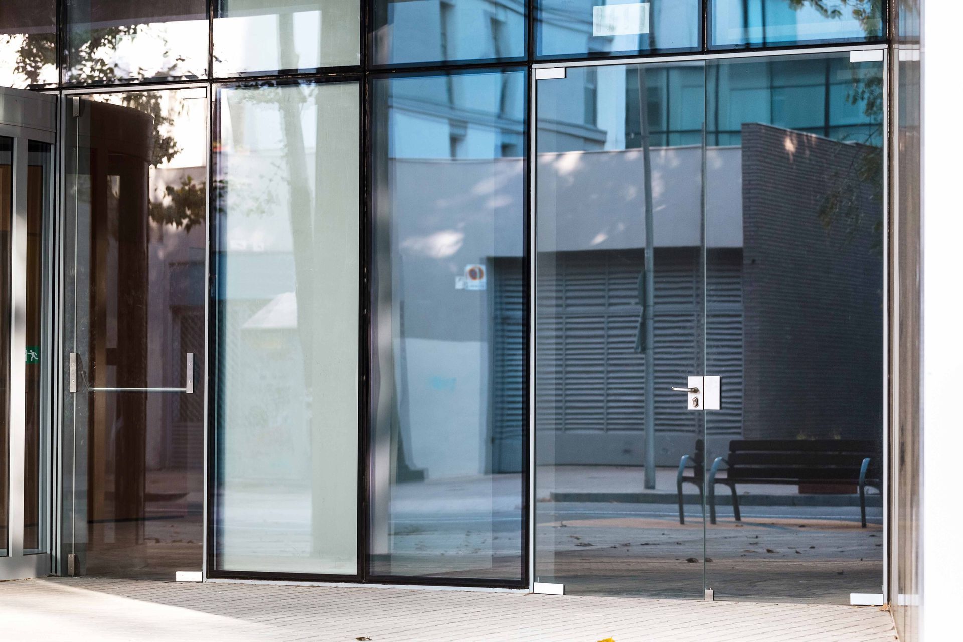 Modern glass storefront with large transparent panels and a glass door reflecting nearby buildings.