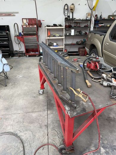 Welded metal ladder frame on a red table in a workshop, tools in the background.