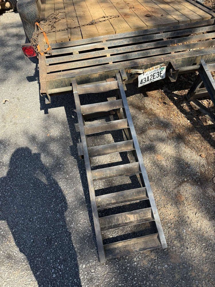 A wooden ramp leans against a flatbed trailer. The ramp is brown, the trailer is metal. Shadows fall across the scene.