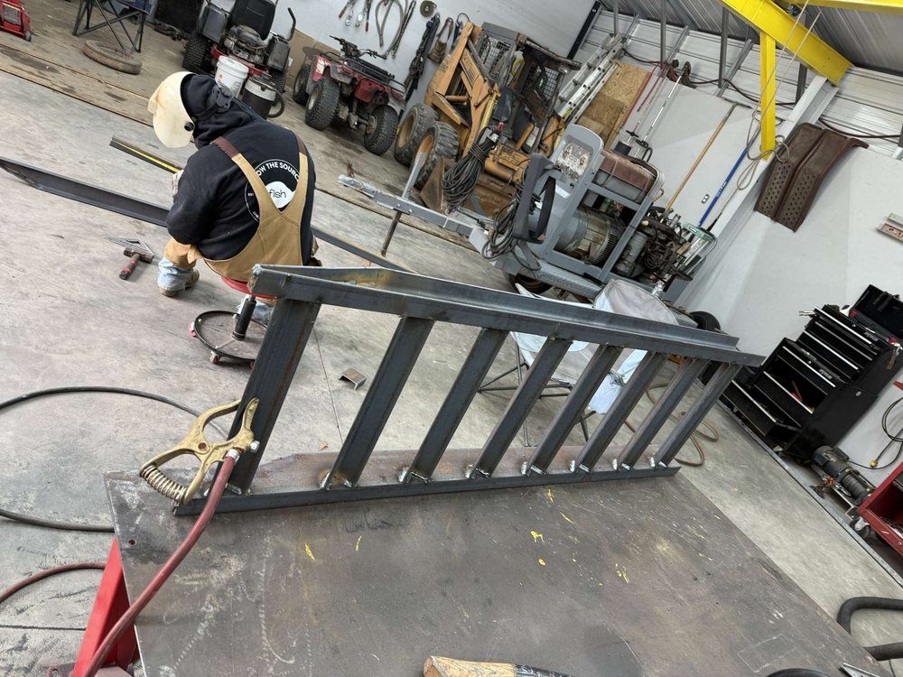 A person welds a metal ladder frame in a workshop, with tools and equipment in the background.