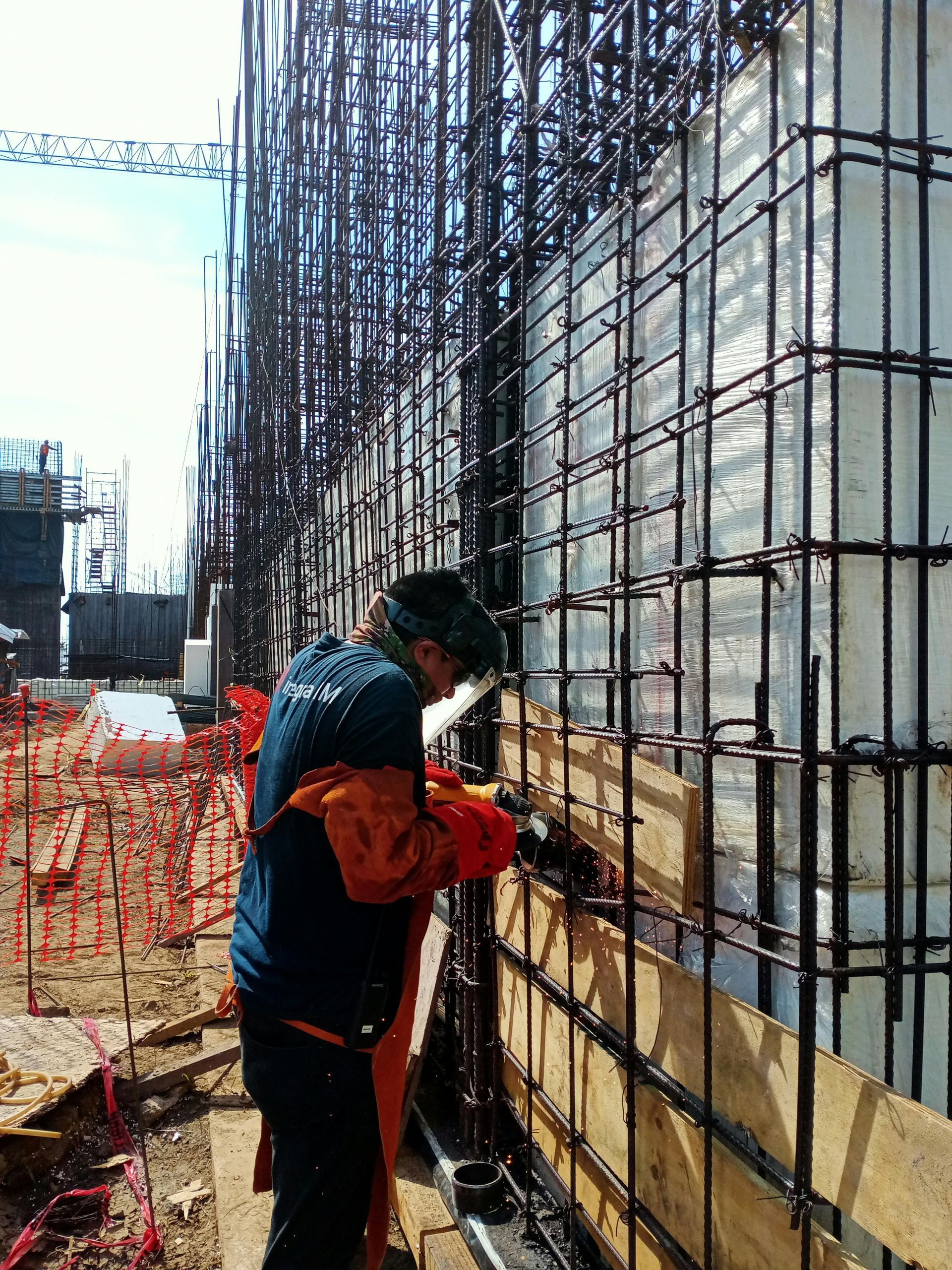 Construction worker welding rebar framework on a building site, wearing safety gear.
