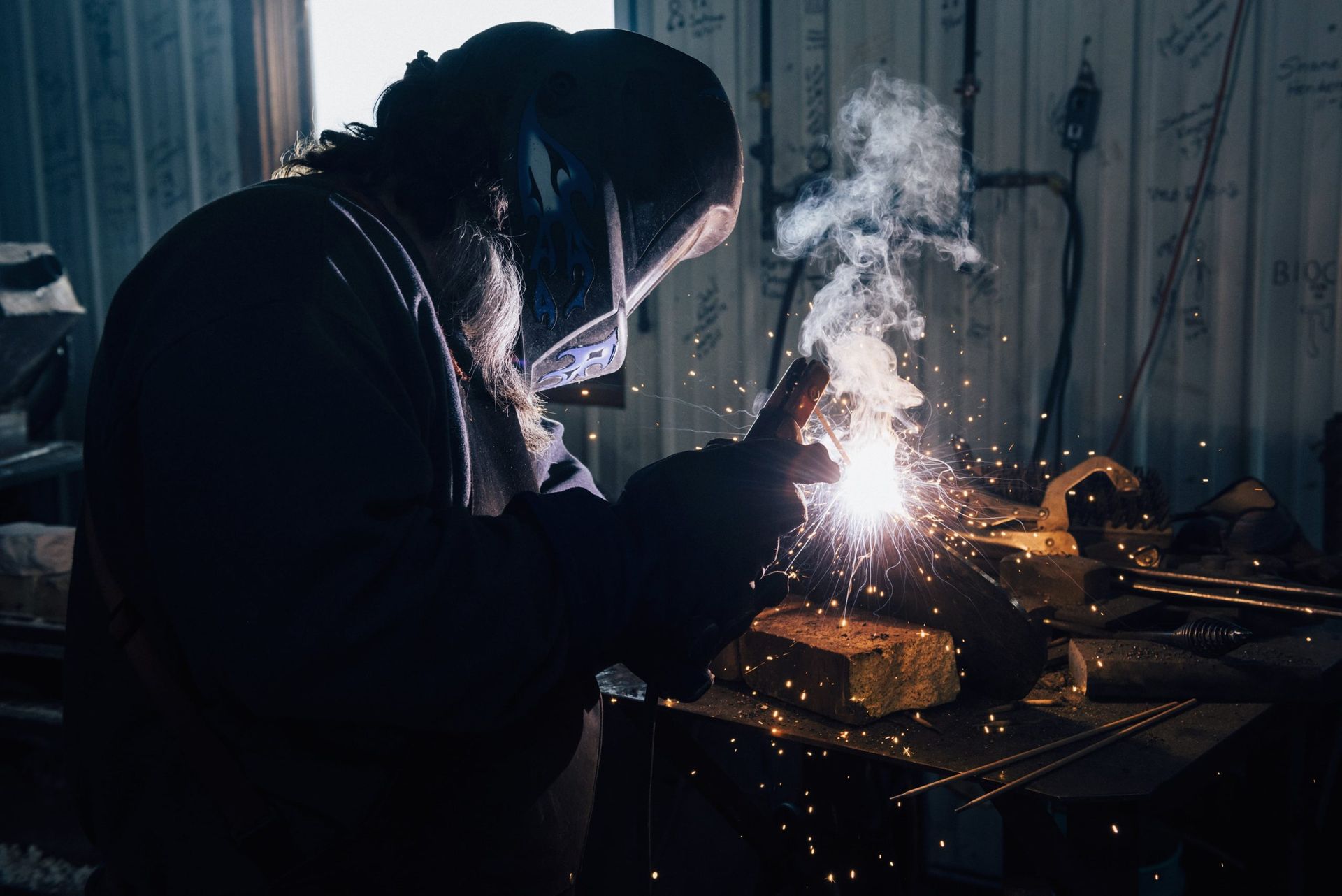 Person welding metal, sparks and smoke visible in a workshop.