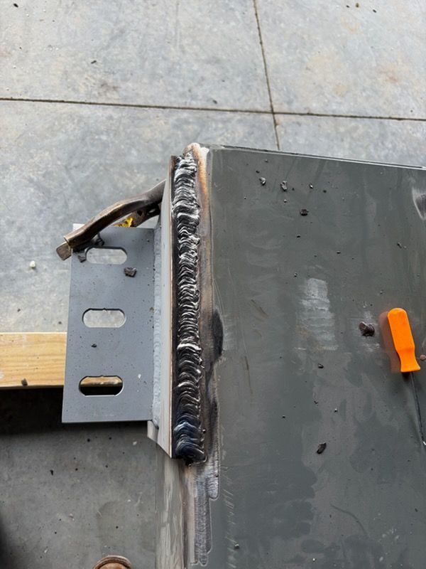 Welded metal pieces: vertical weld bead on a gray metal bracket attached to a larger painted metal structure.