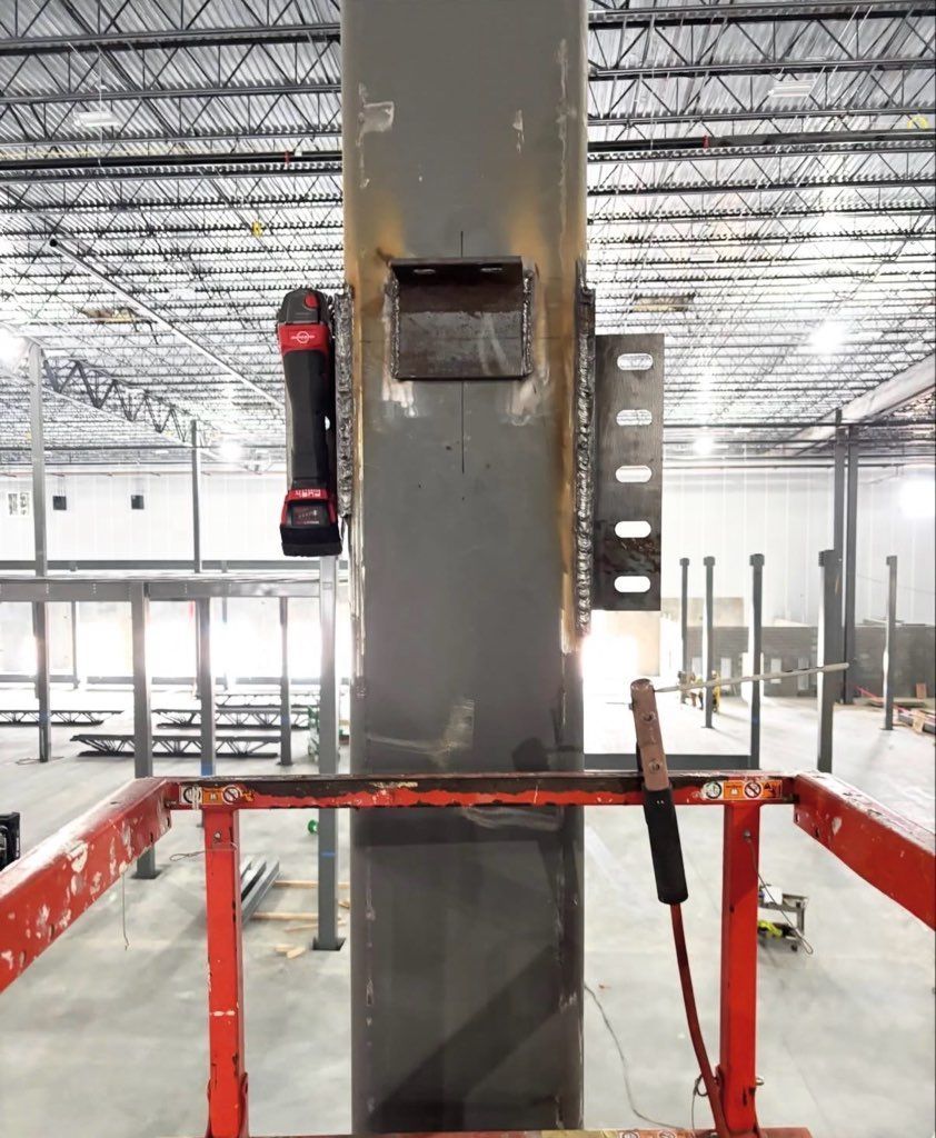 Construction worker on lift welding steel beam to a grey metal column inside a building.