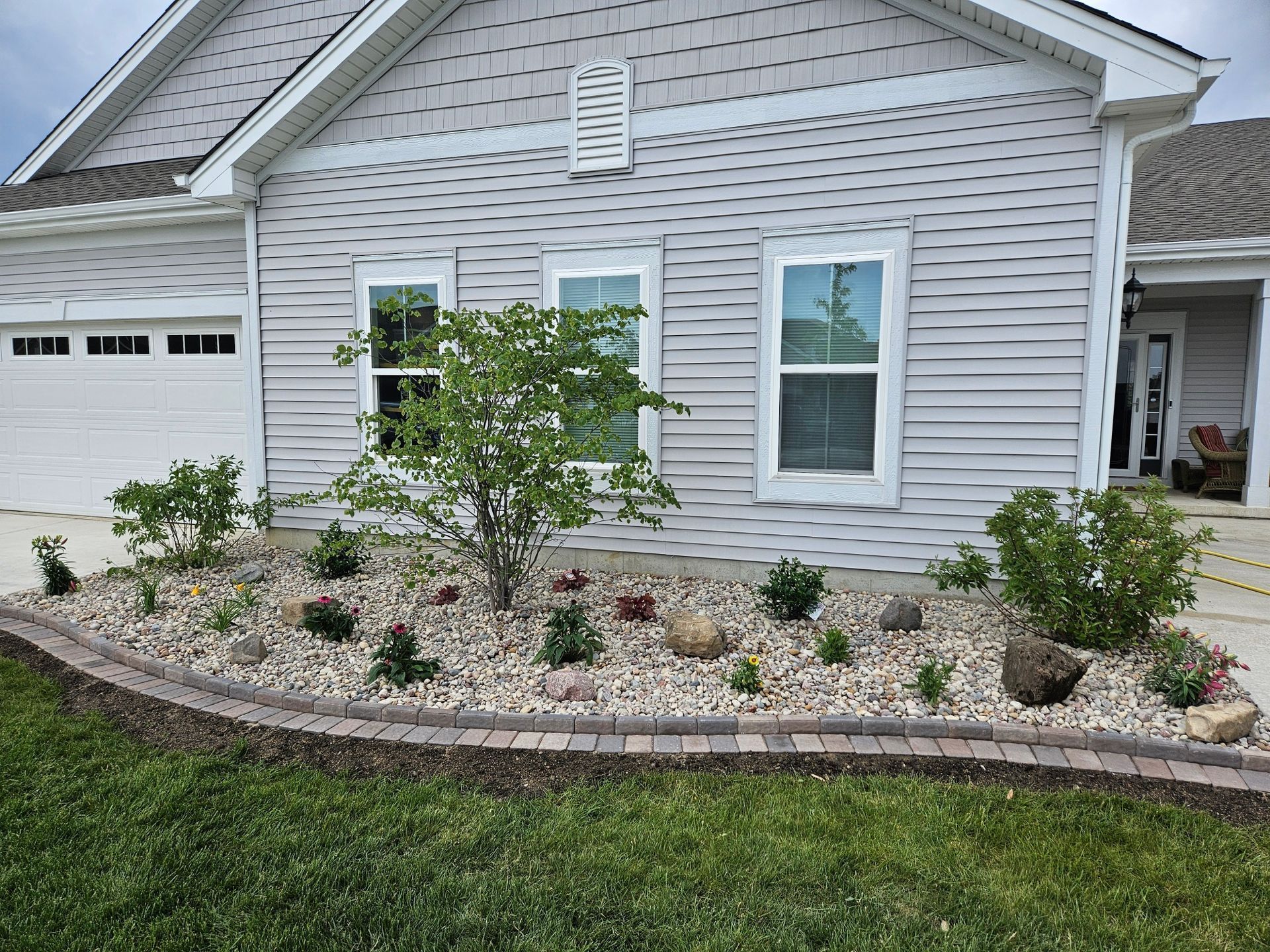 Front of a gray house with white shutters and a landscaped rock garden along the foundation.