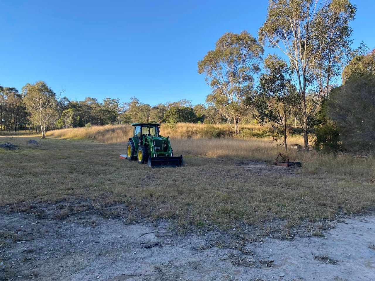 A green tractor is parked in a field with trees in the background. — Hilltop Property Services In Crows Nest, QLD 