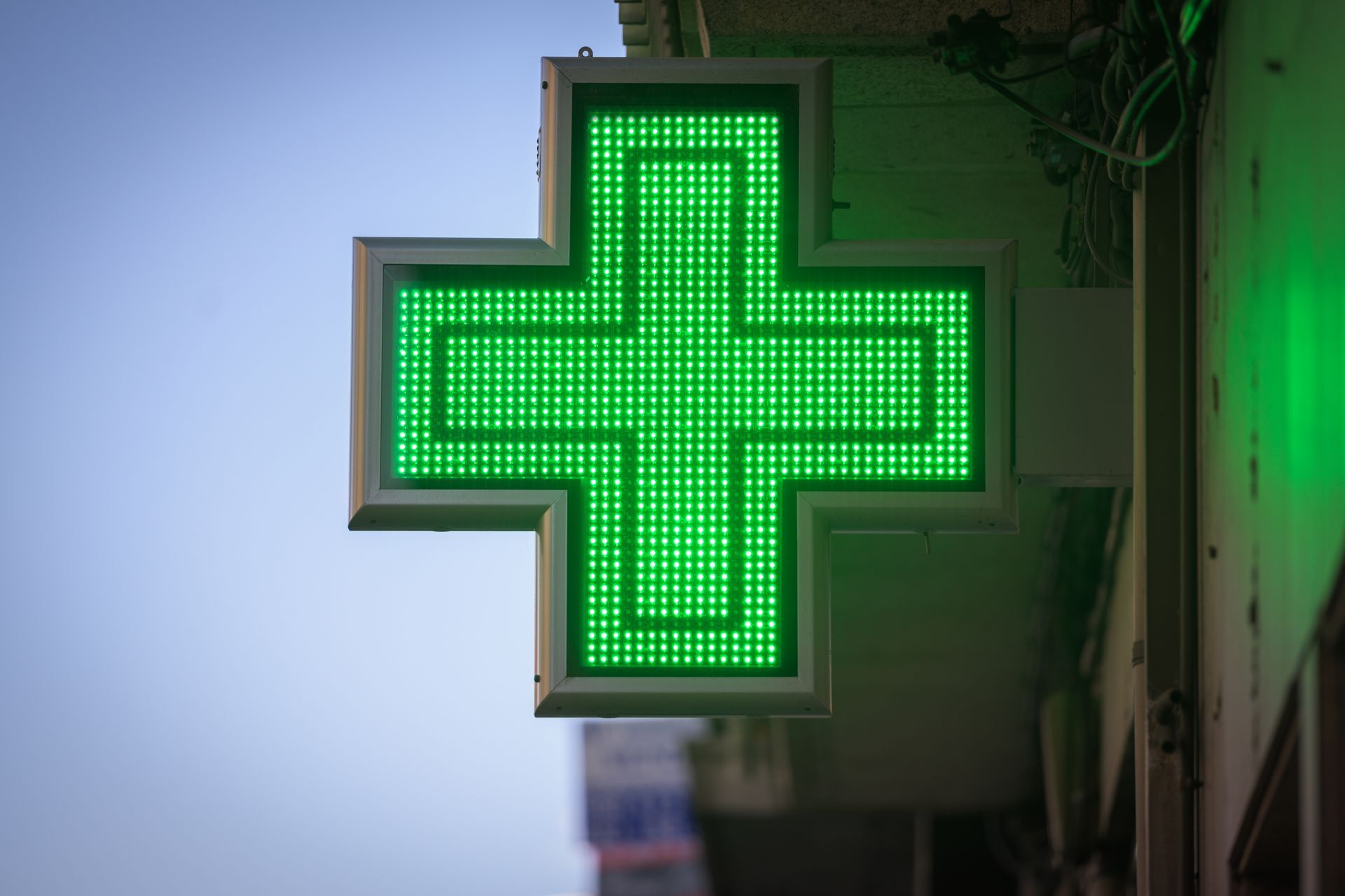Insegna al neon verde con croce di farmacia su un edificio.