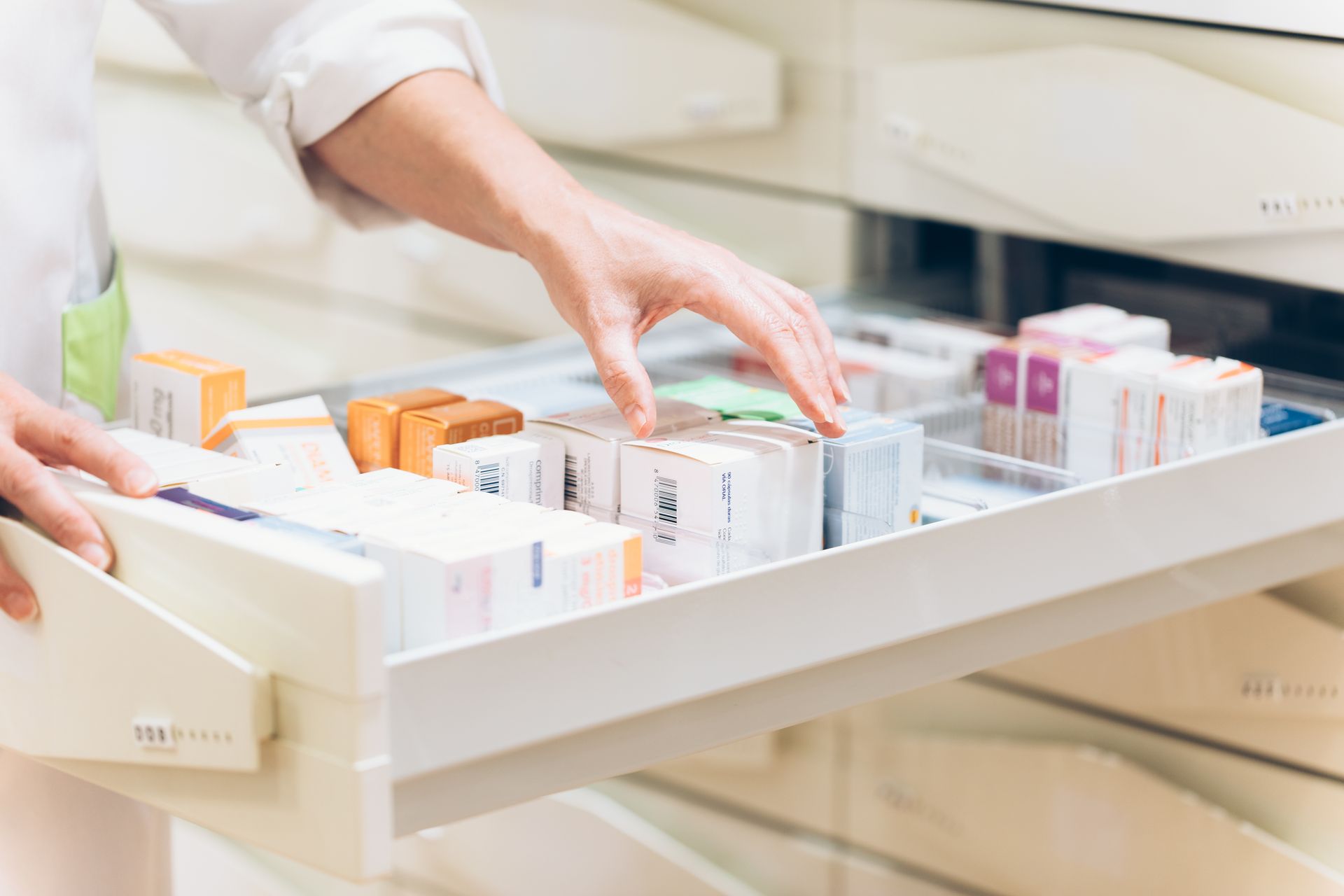 Le mani di un farmacista che frugano in un cassetto pieno di scatole di medicinali in una farmacia.