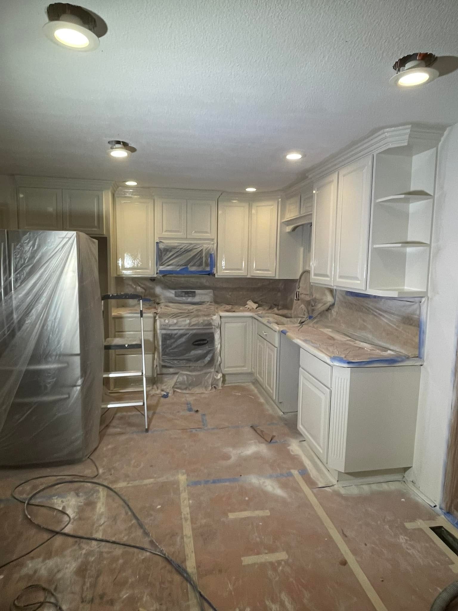A kitchen with white cabinets and a refrigerator is being painted.