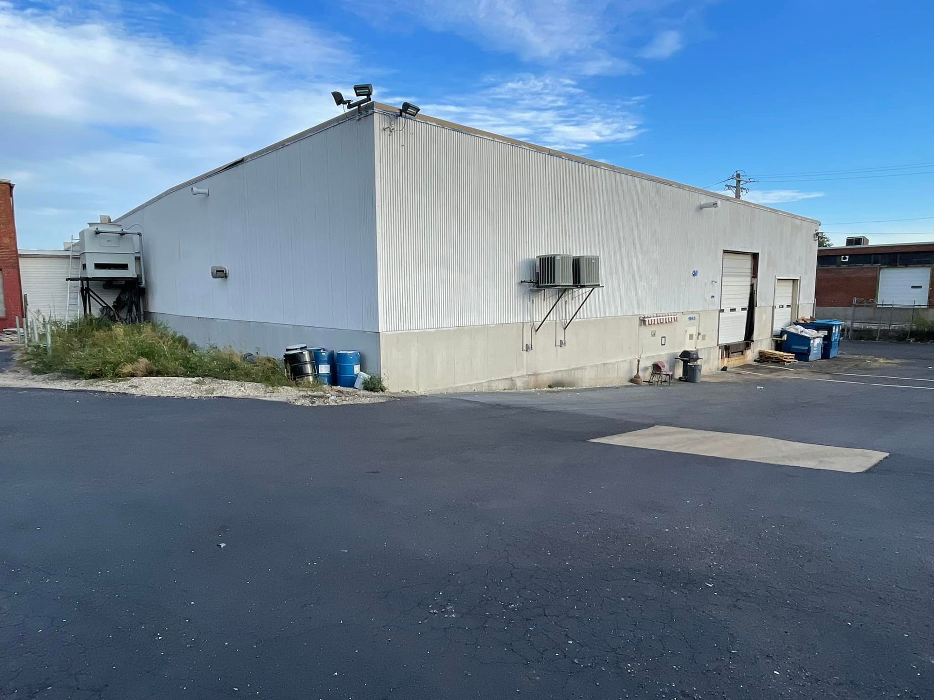 A white building with a blue barrel in front of it.