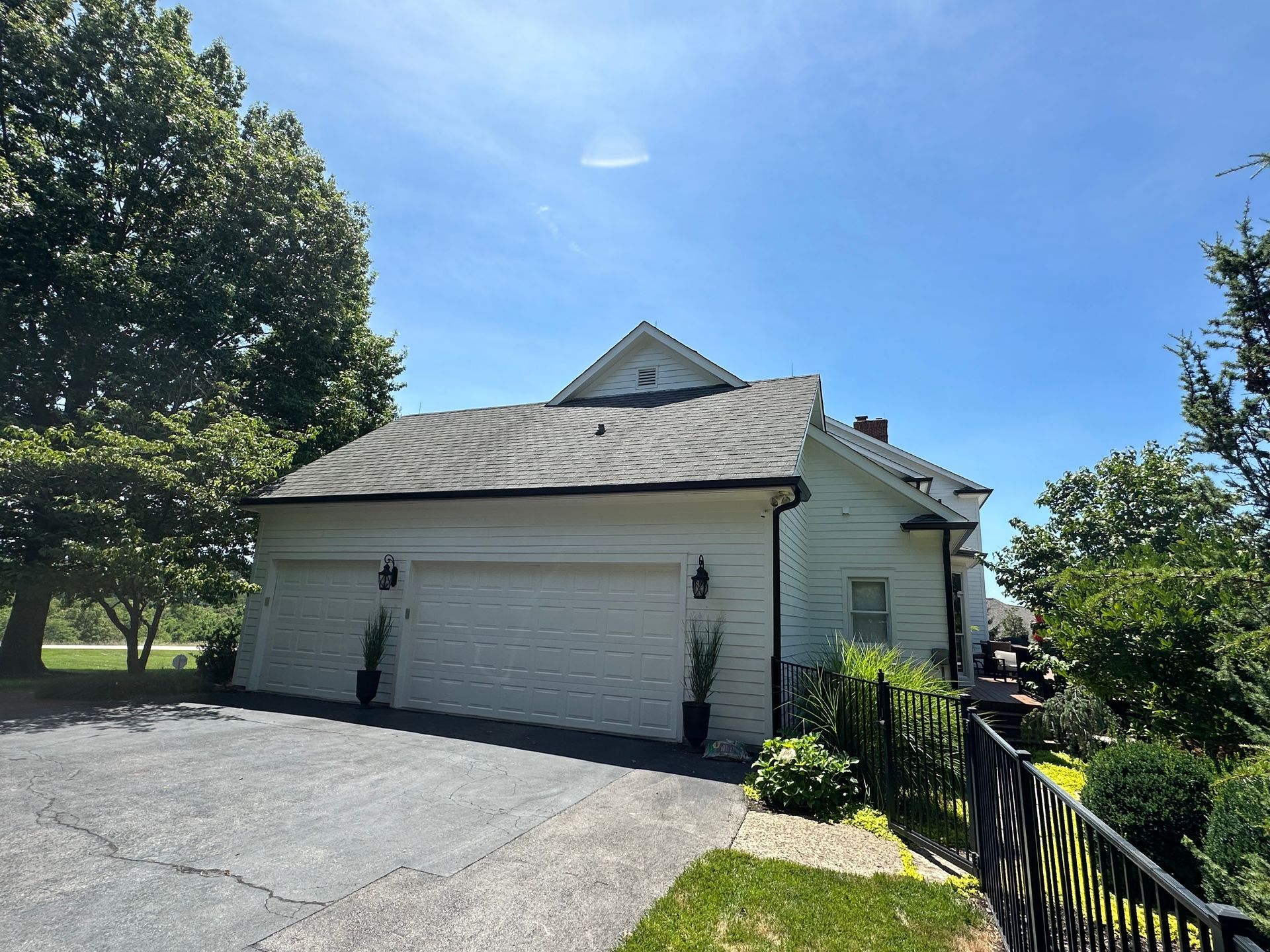 A white house with two garage doors and a fence in front of it.