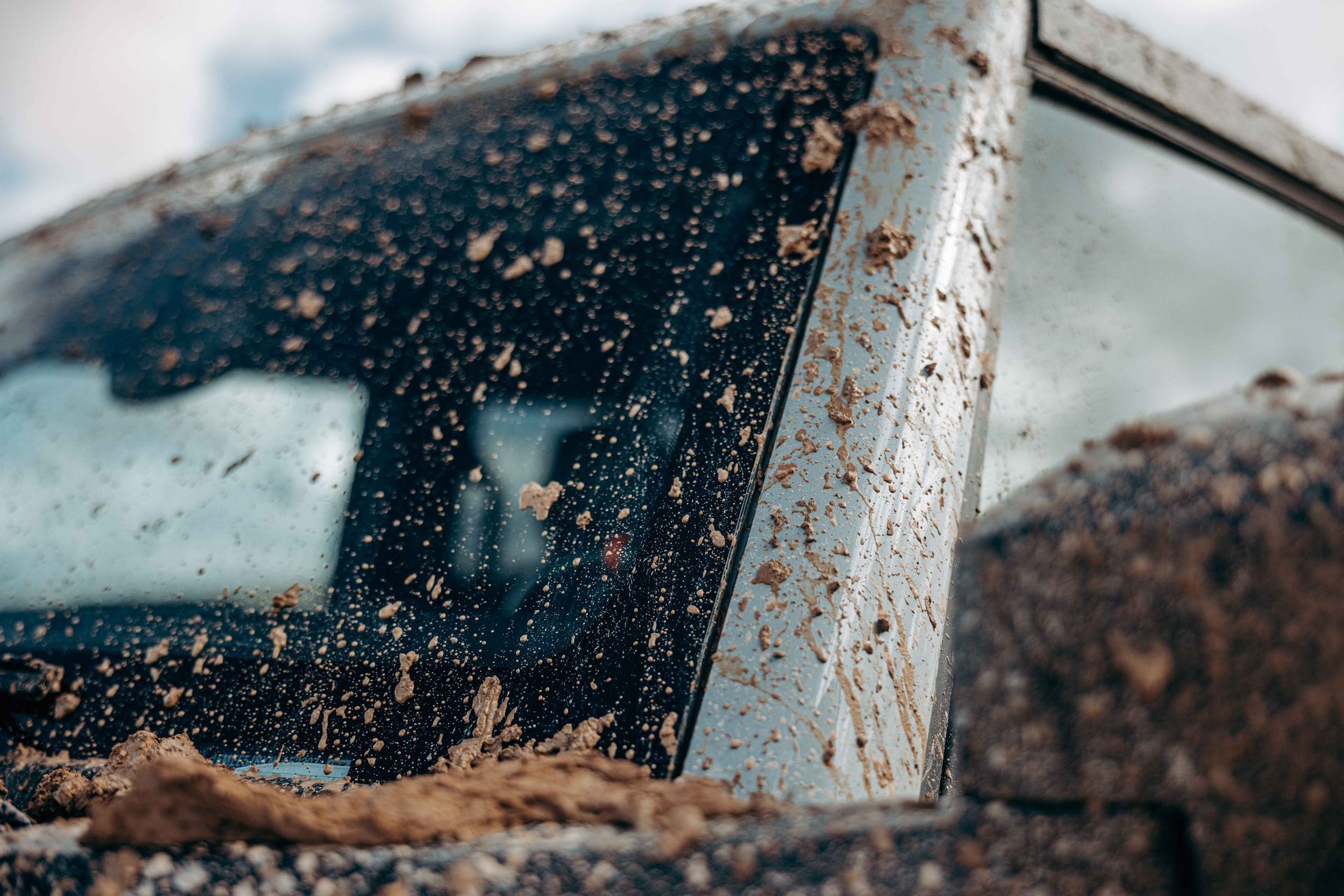Mud-splattered car window and door frame, outdoors, possibly after off-roading.
