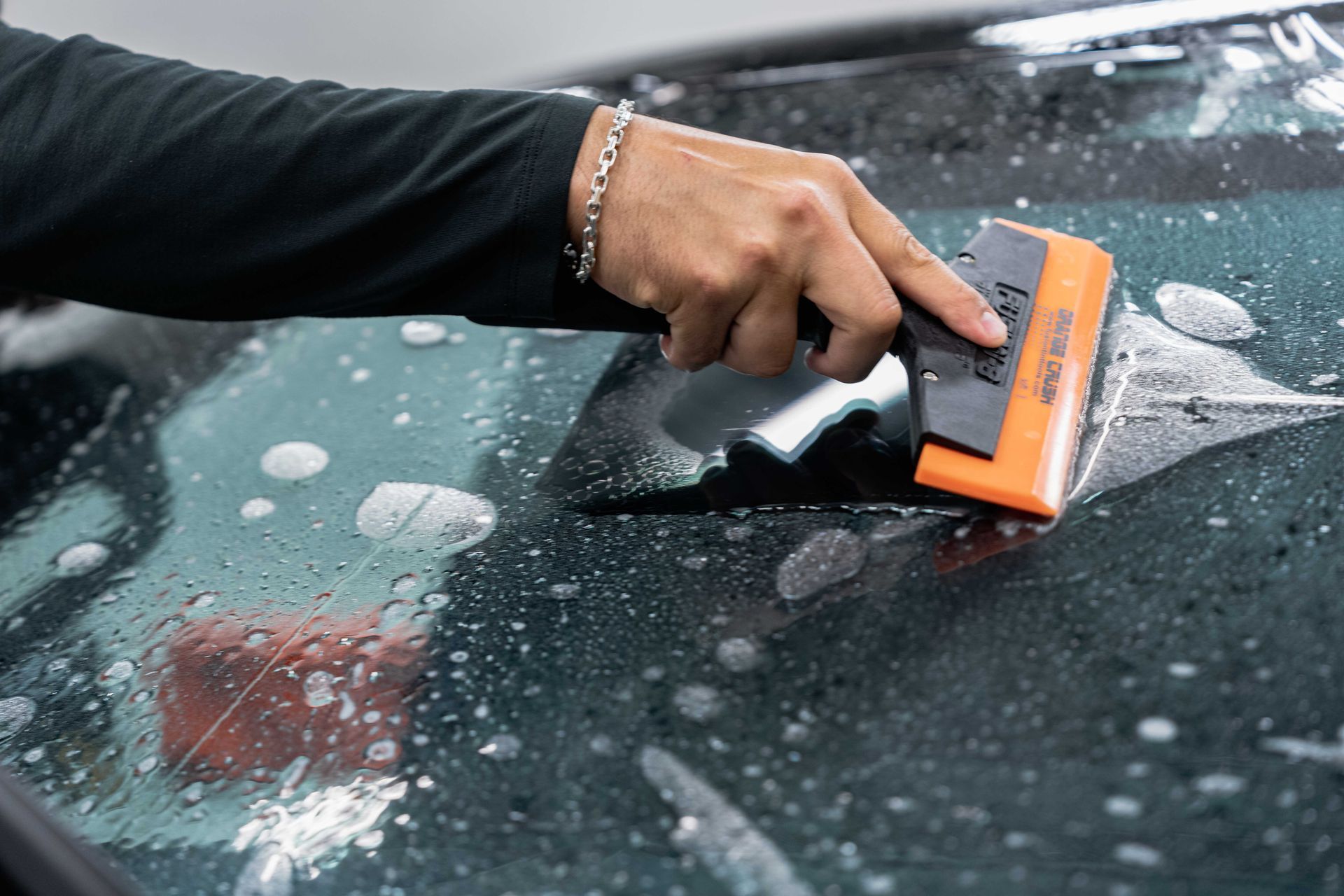 Person applying window tint to a car windshield using a squeegee.