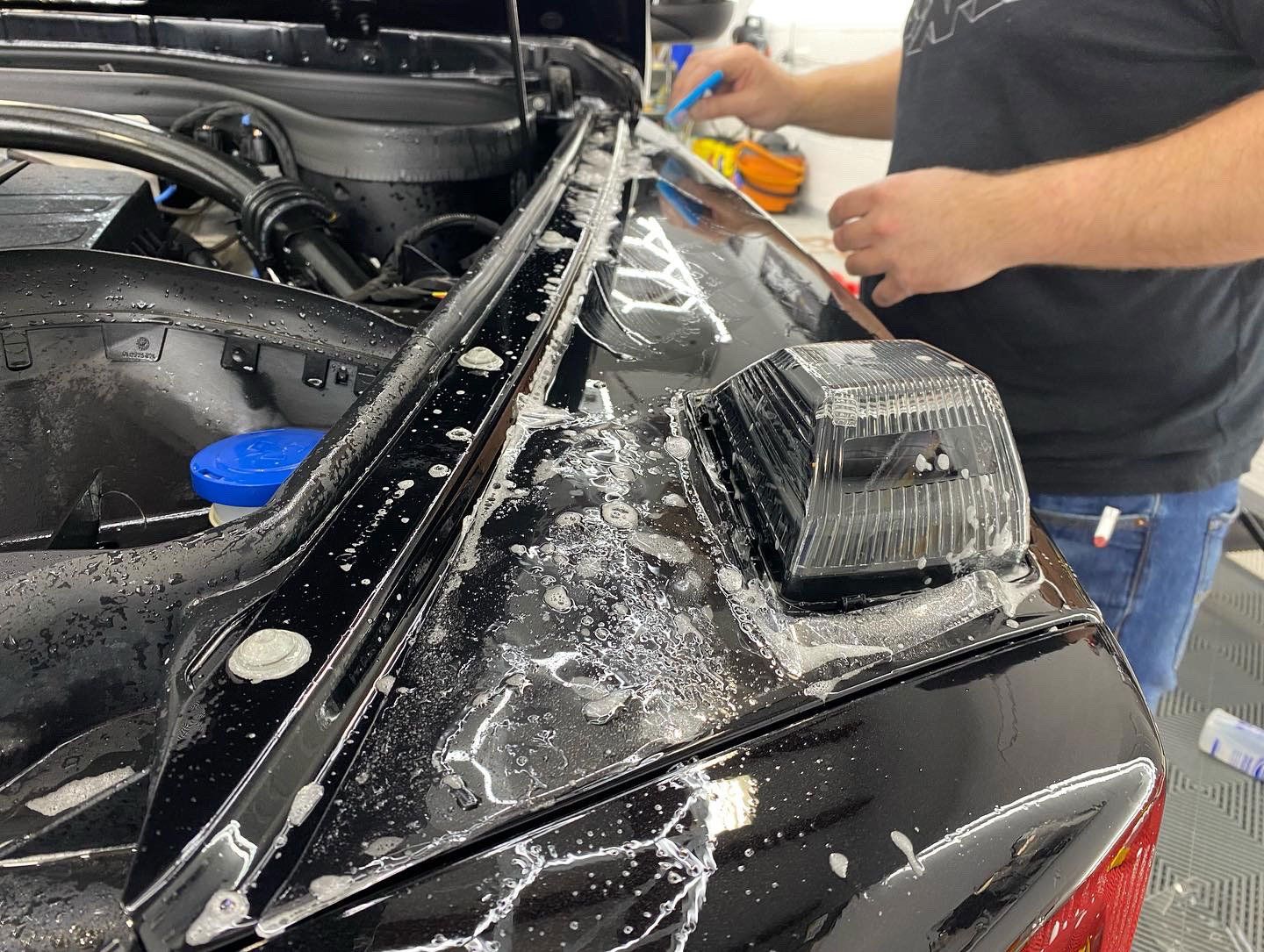 Person applying film to the edge of a black car with soapy water.