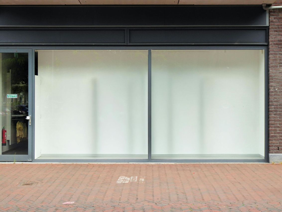 Closed storefront with large white display windows and a brick sidewalk in front
