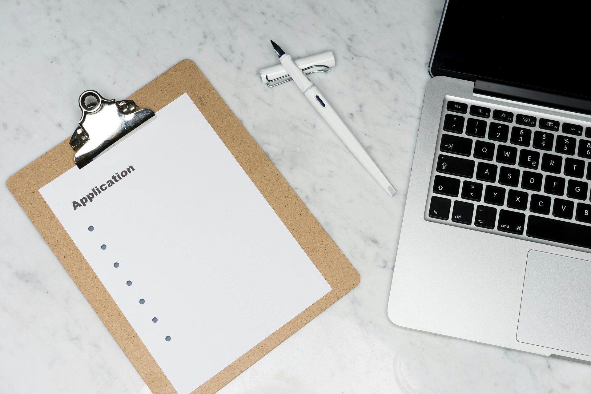Clipboard with blank paper, pen, and laptop on a marble desk