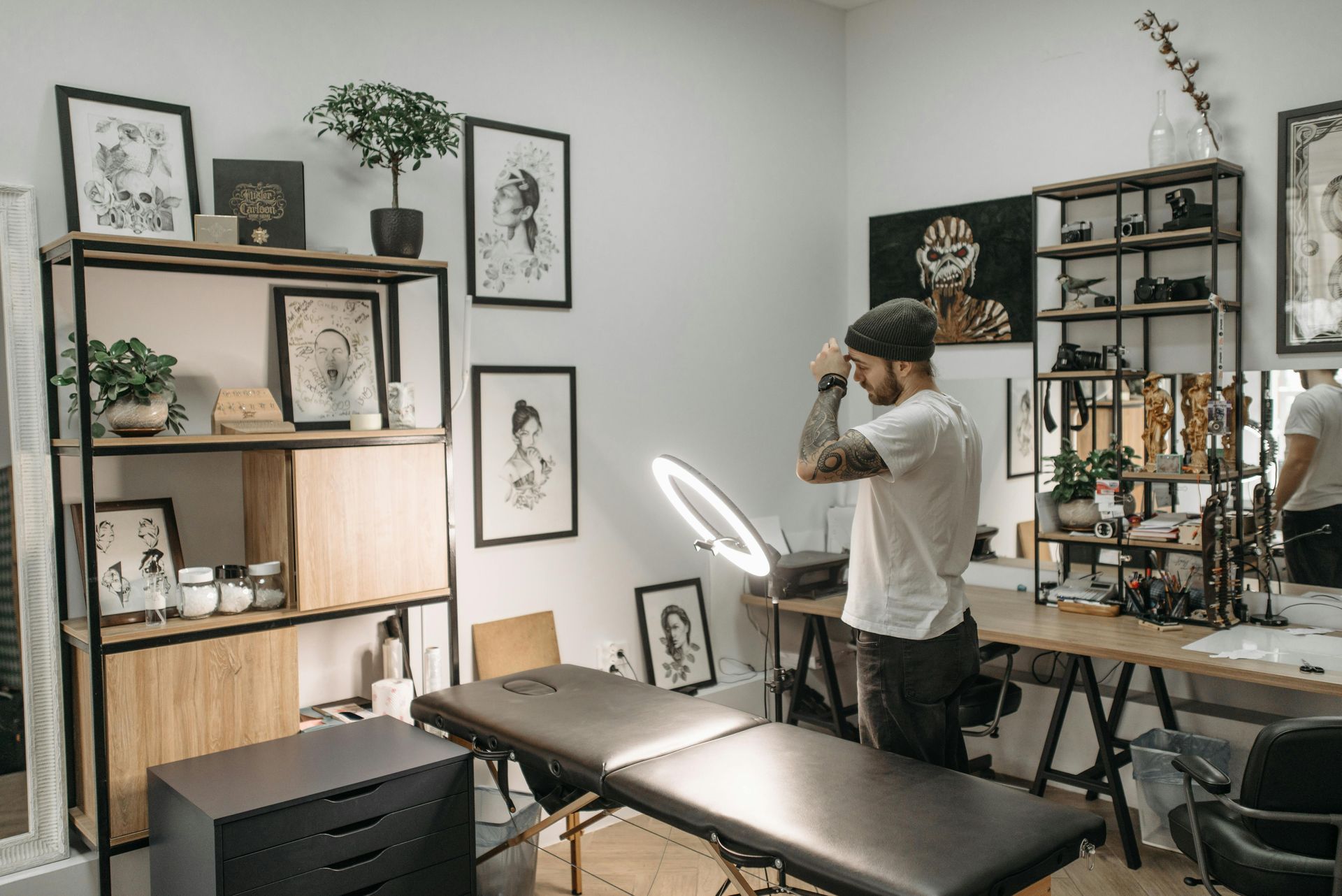 Person setting up a ring light in a minimalist tattoo studio with shelves and framed art