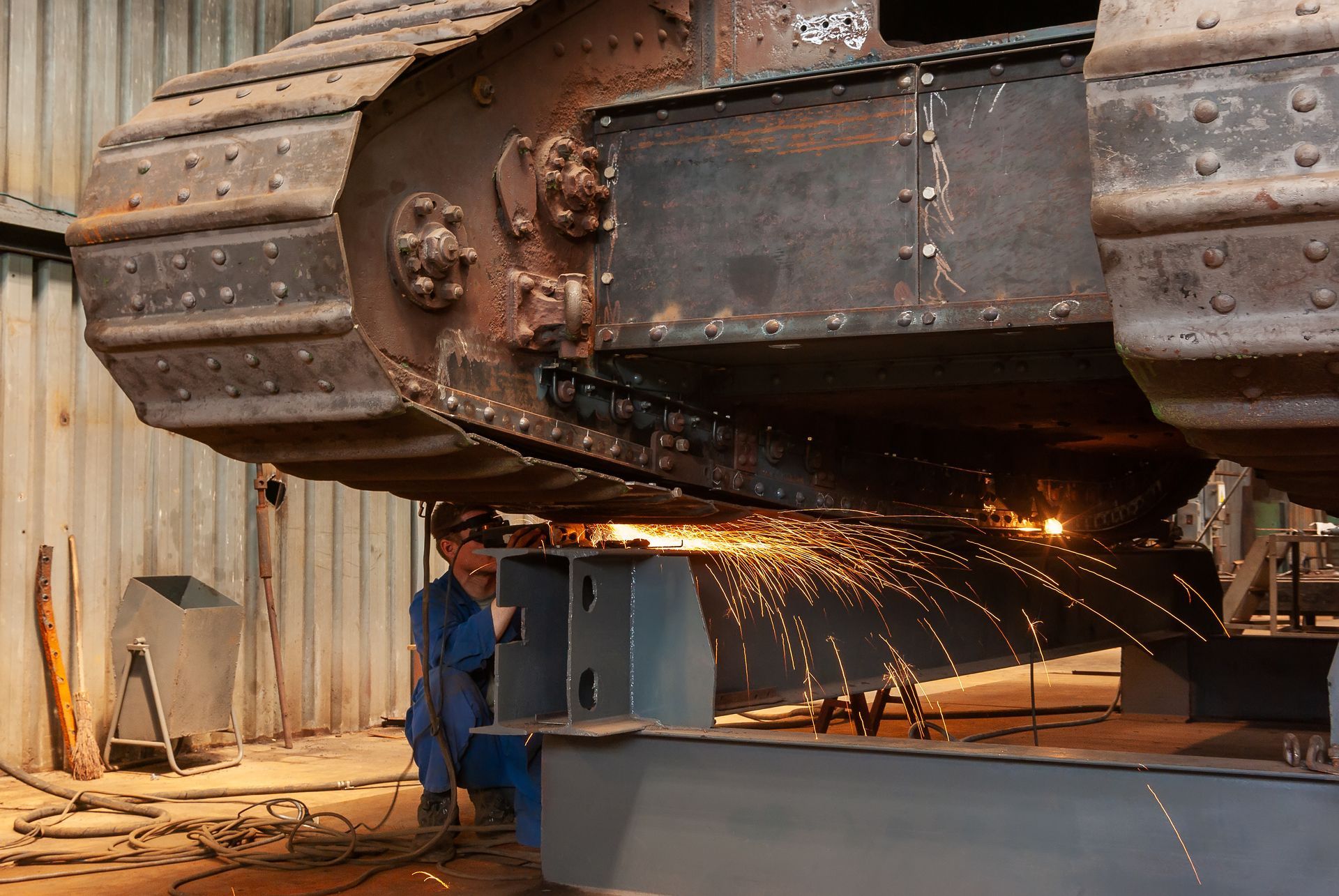 A worker is welding an old, armored tank in a factory workshop.